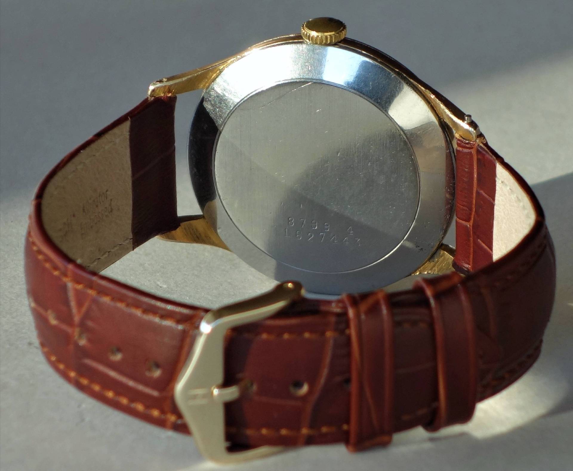 Armbanduhr mit braunem Armband und silberfarbener Rückseite.