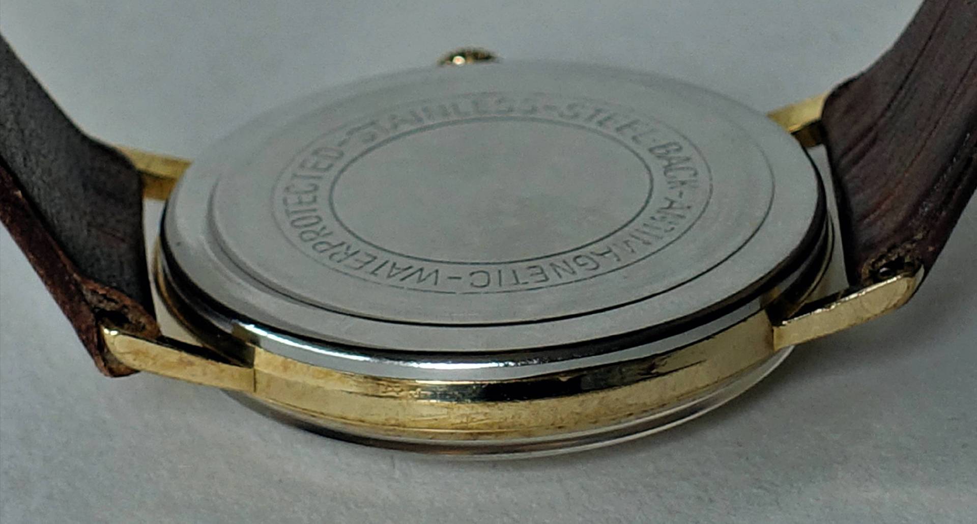 Runder, silberfarbener Uhrenboden mit umlaufender Gravur an einer Armbanduhr.