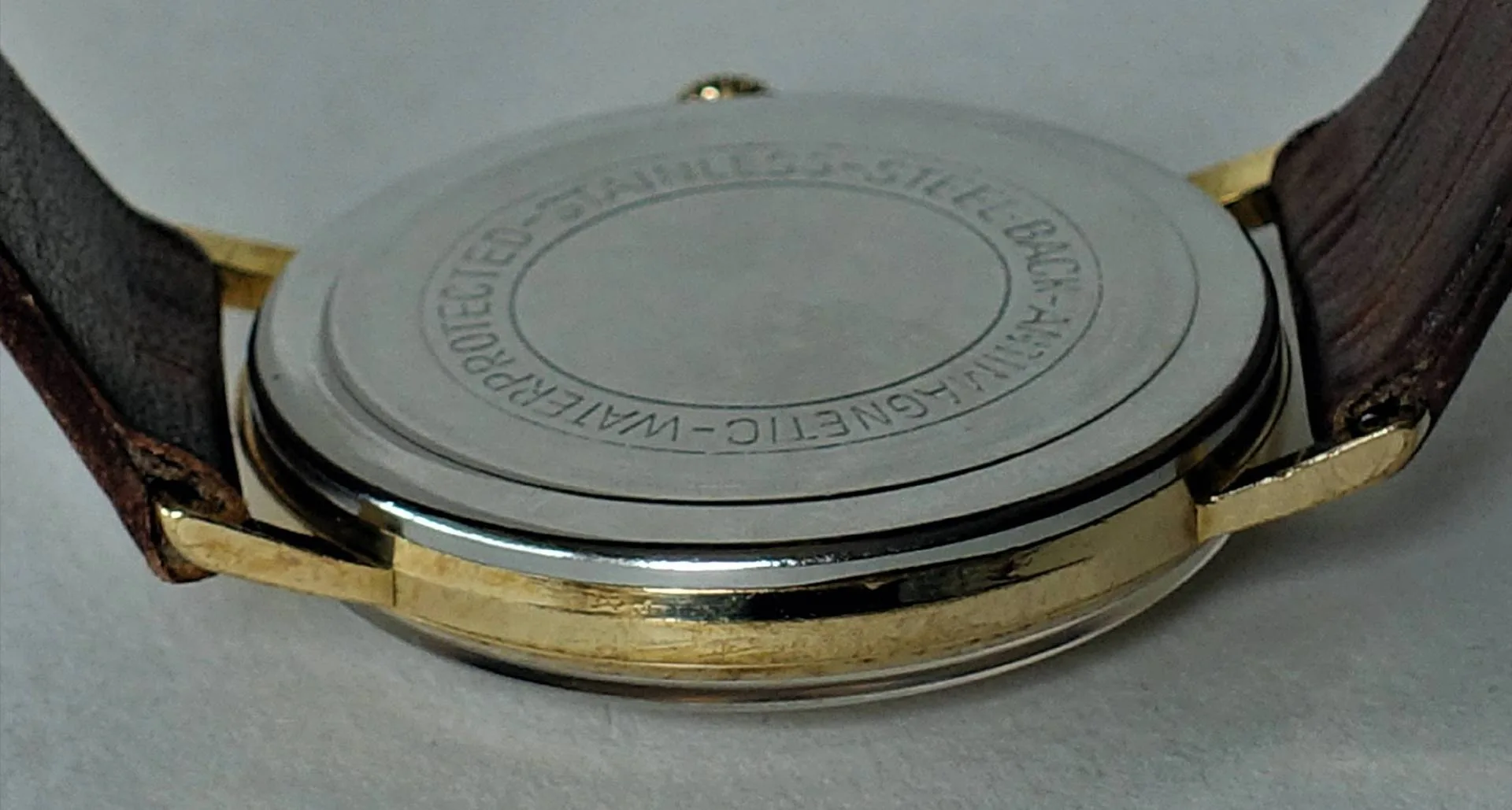 Runder, silberfarbener Uhrenboden mit umlaufender Gravur an einer Armbanduhr.