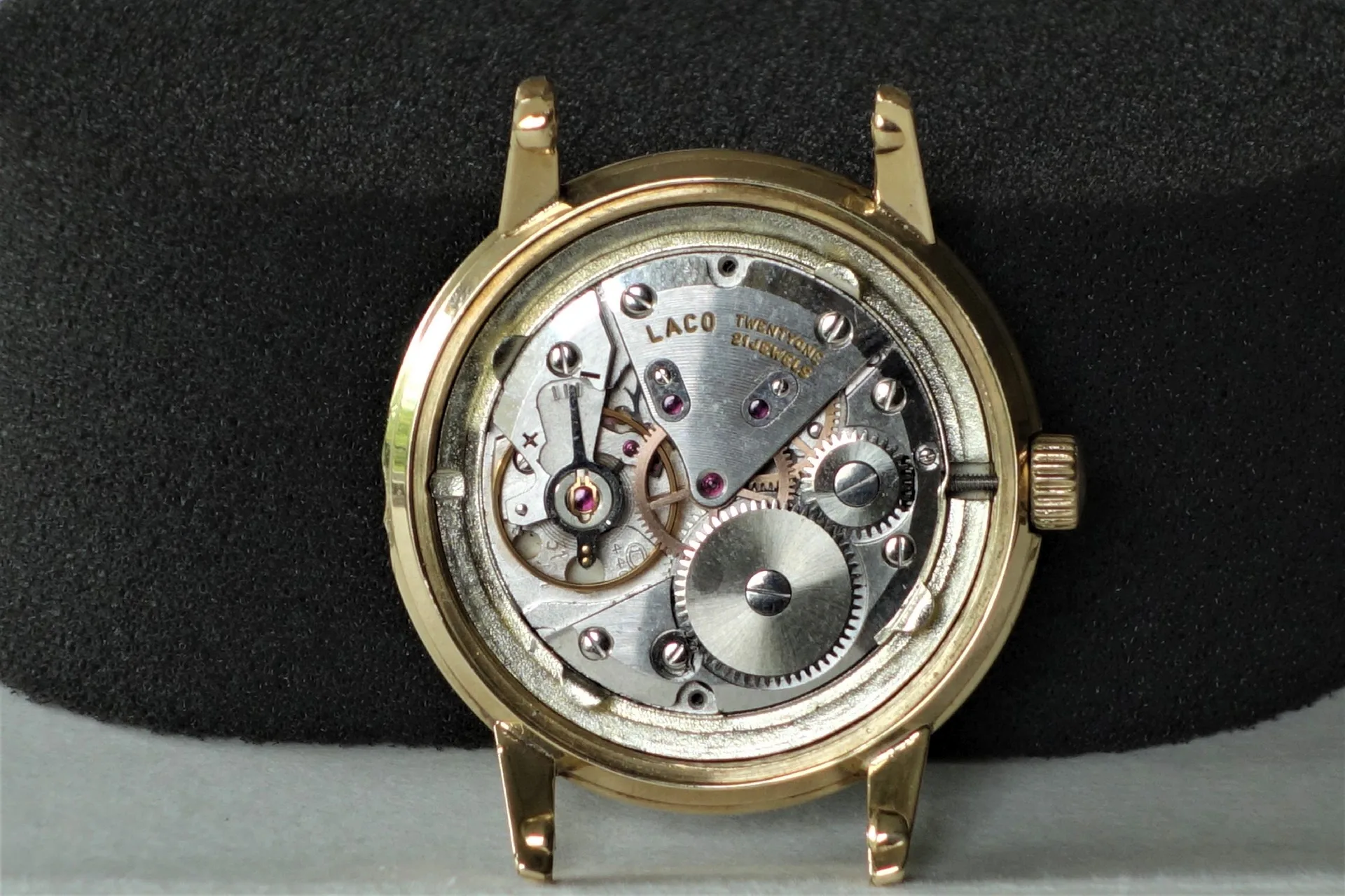 Mechanisches Uhrwerk im Gehäuse Mechanisches Uhrwerk in einem goldfarbenen Uhrengehäuse mit sichtbaren Zahnrädern und Aufzugswelle.