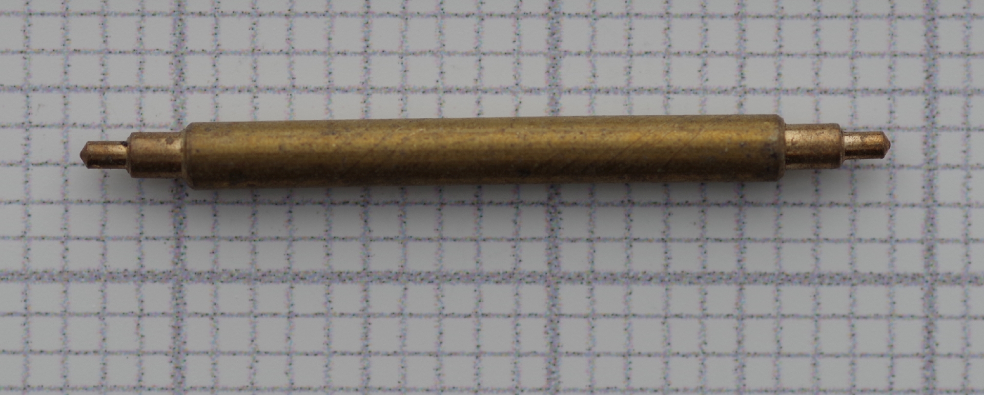 Zylinderförmige Aufzugswelle aus Messing für mechanische Uhren, auf kariertem Hintergrund.