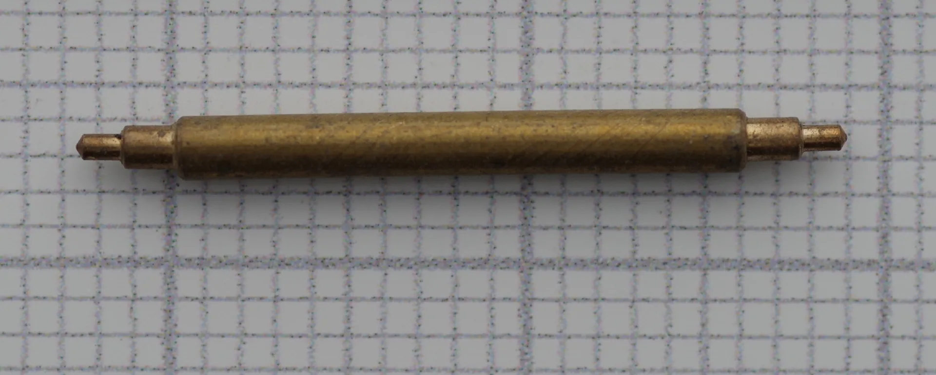 Zylinderförmige Aufzugswelle aus Messing für mechanische Uhren, auf kariertem Hintergrund.