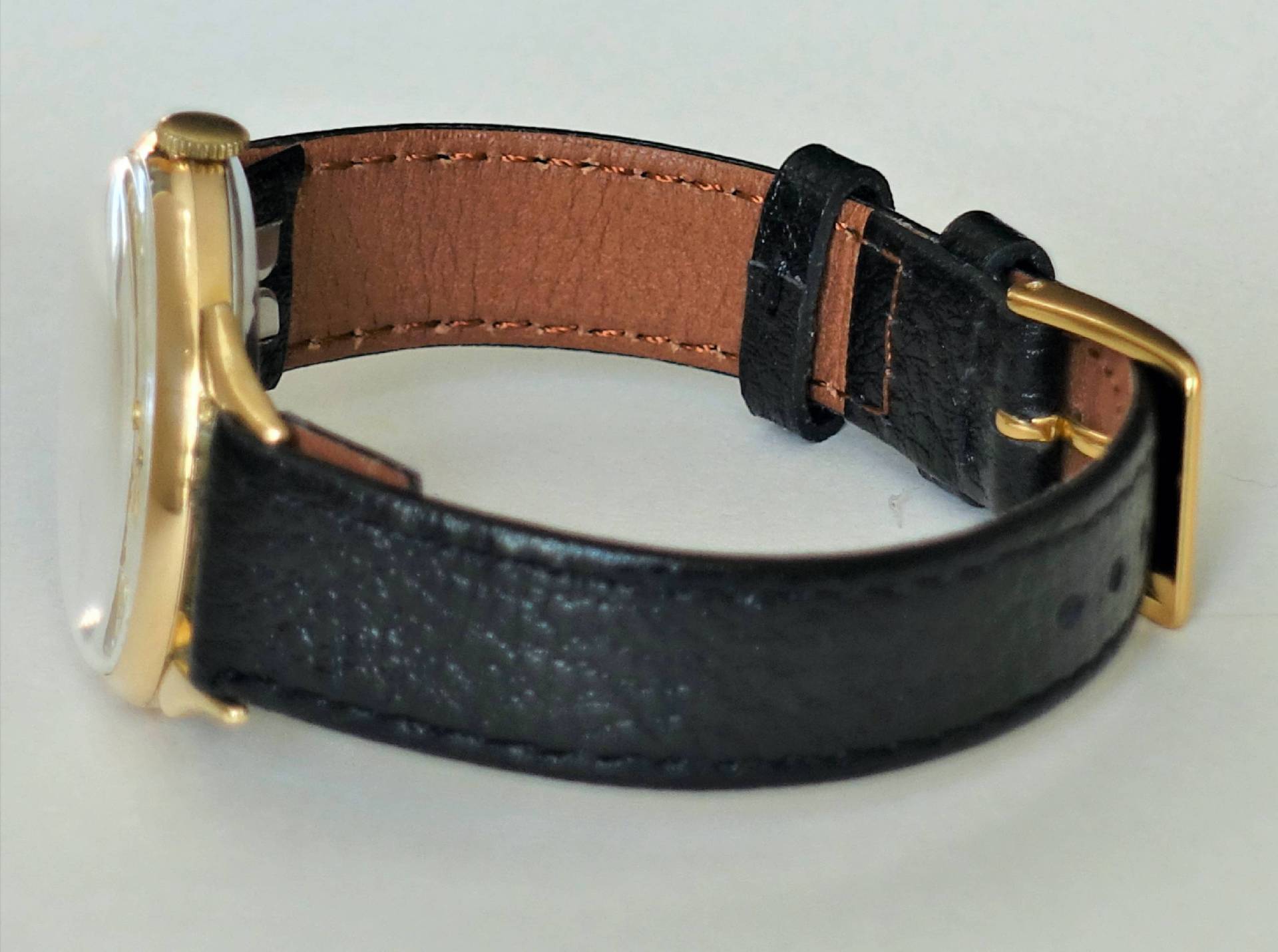 Armbanduhr mit schwarzem Armband und goldfarbenem Gehäuse sowie Schließe.