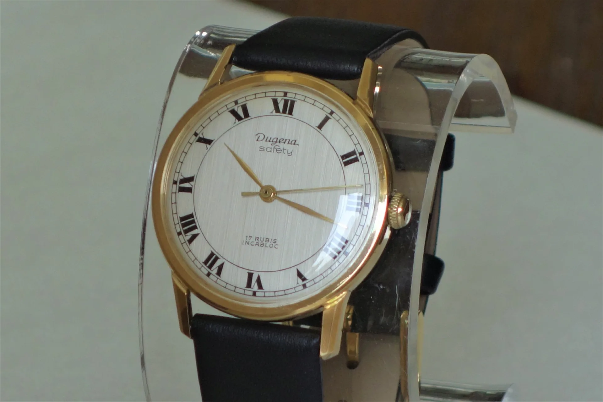 Dugena Armbanduhr goldfarben Klassische Armbanduhr mit goldfarbenem Gehäuse, weißem Zifferblatt mit römischen Zahlen und schwarzem Armband.