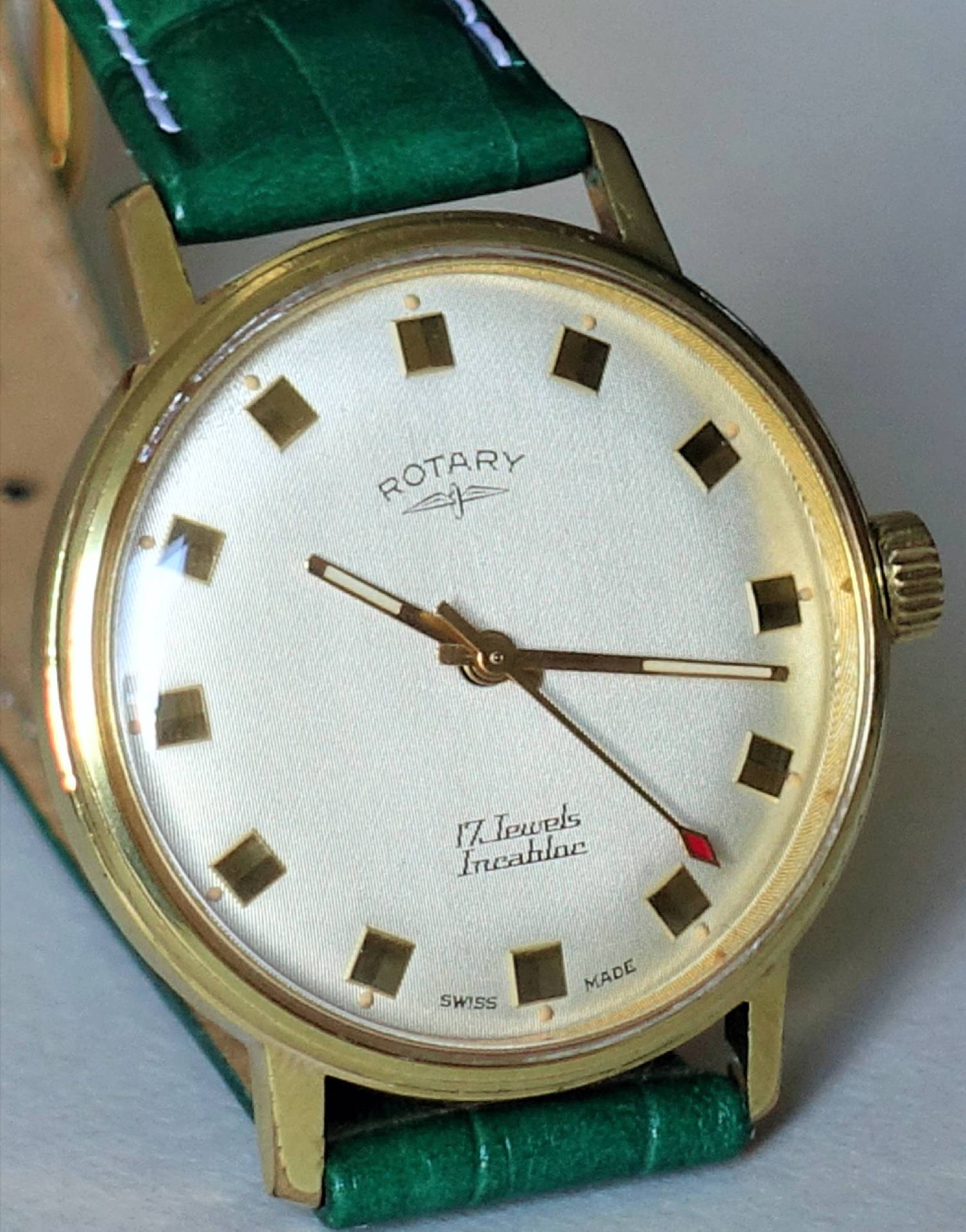 Analoge Armbanduhr mit goldfarbenem Gehäuse, weißem Zifferblatt und grünem Armband.