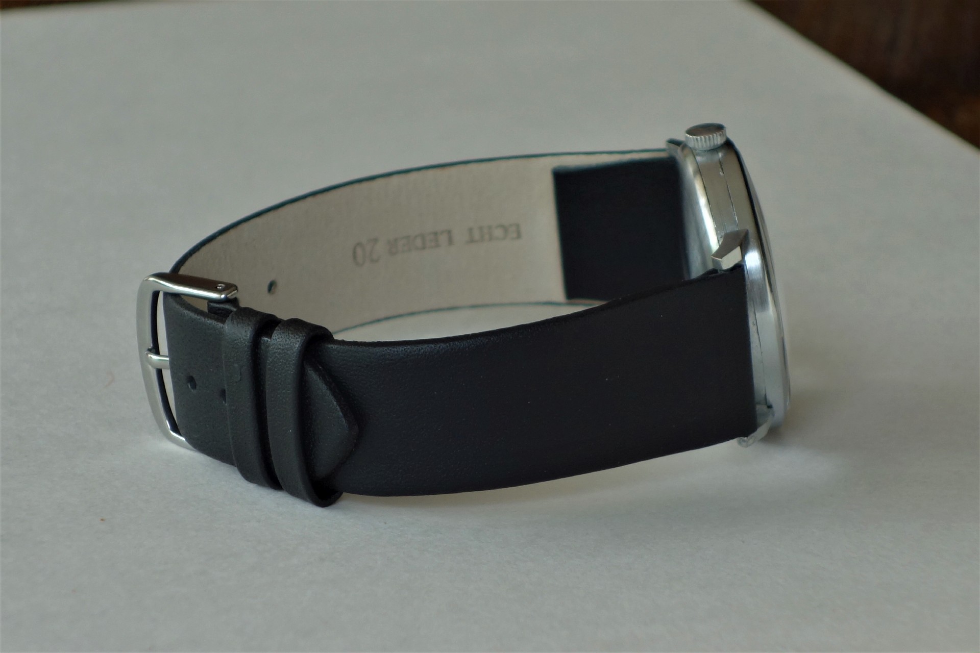 Schwarzes Lederarmband mit silberfarbener Dornschließe an einer Armbanduhr.