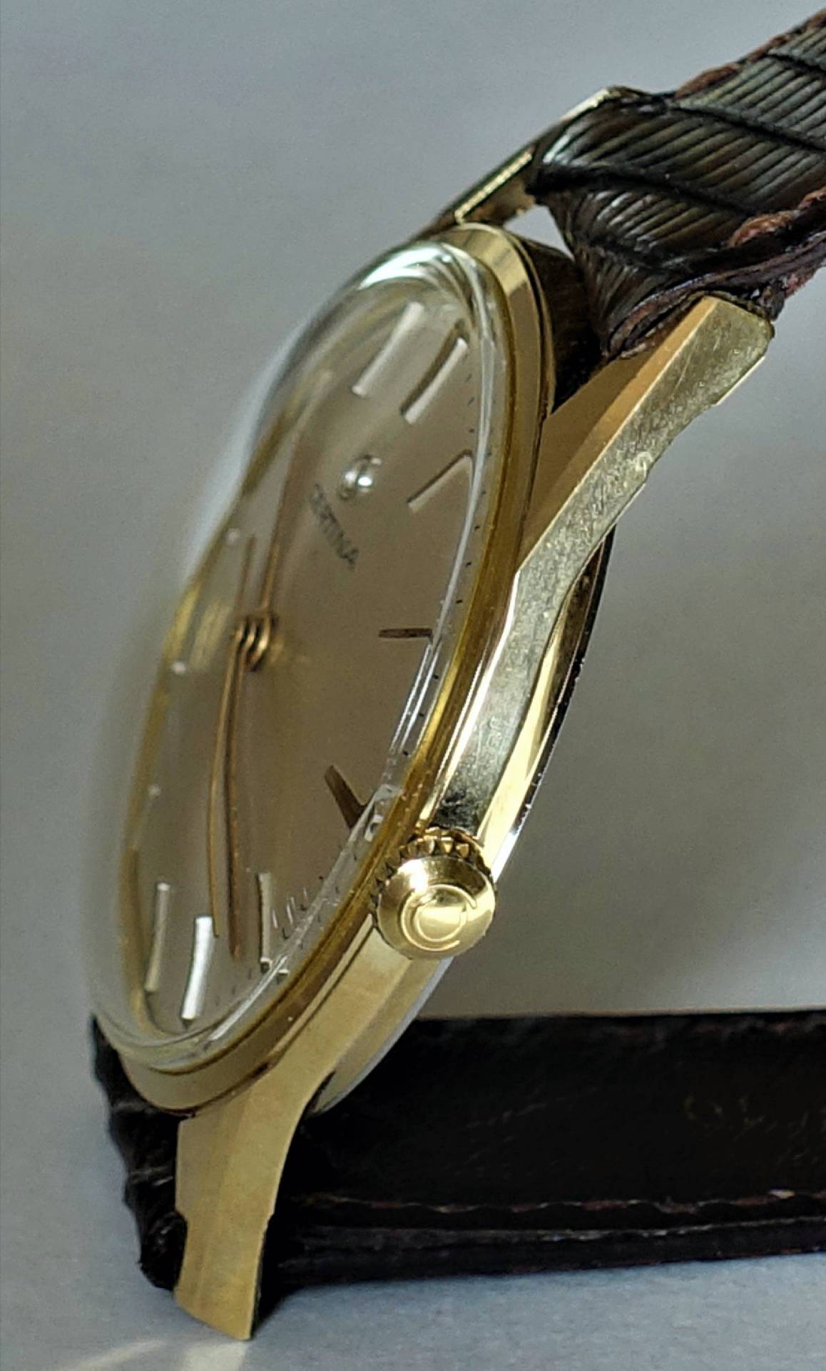 Flache Armbanduhr mit goldfarbenem Gehäuse und braunem Armband.