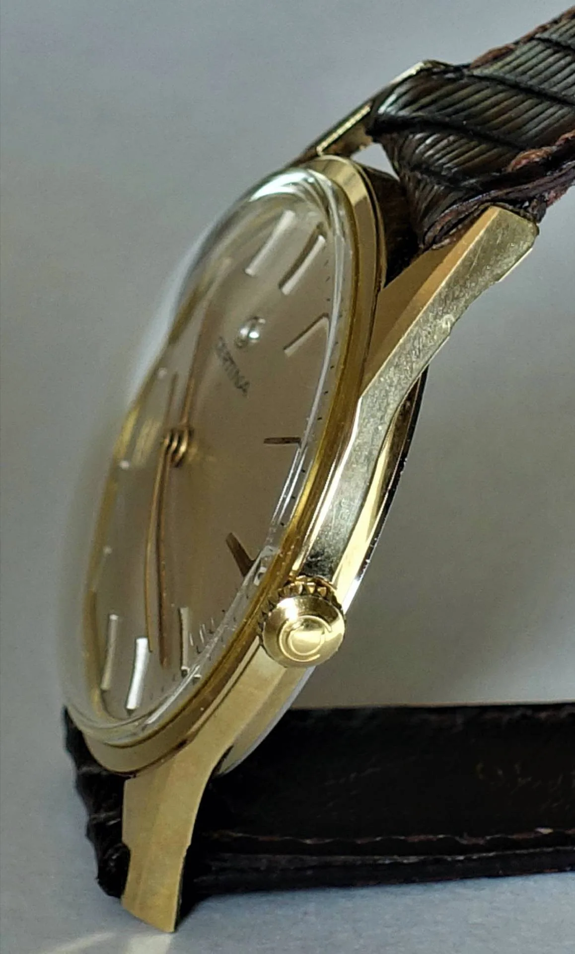 Flache Armbanduhr mit goldfarbenem Gehäuse und braunem Armband.