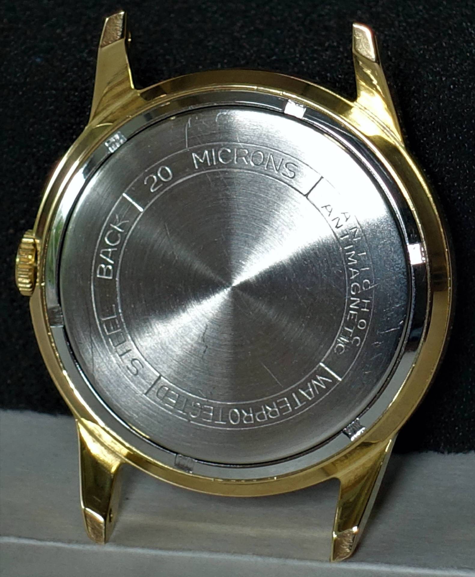 Goldfarbenes Uhrengehäuse mit silberfarbener Rückseite aus Metall.