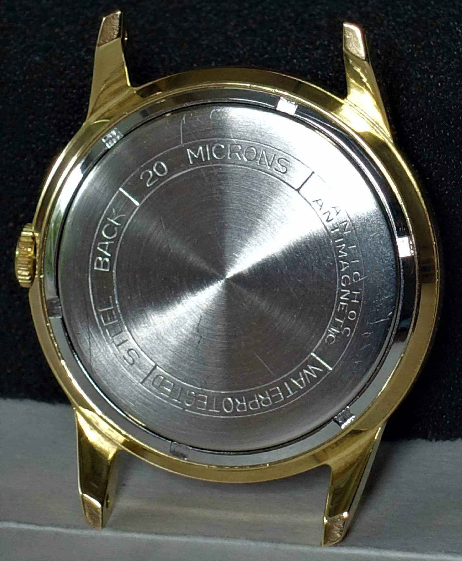 Goldfarbenes Uhrengehäuse mit silberfarbener Rückseite aus Metall.