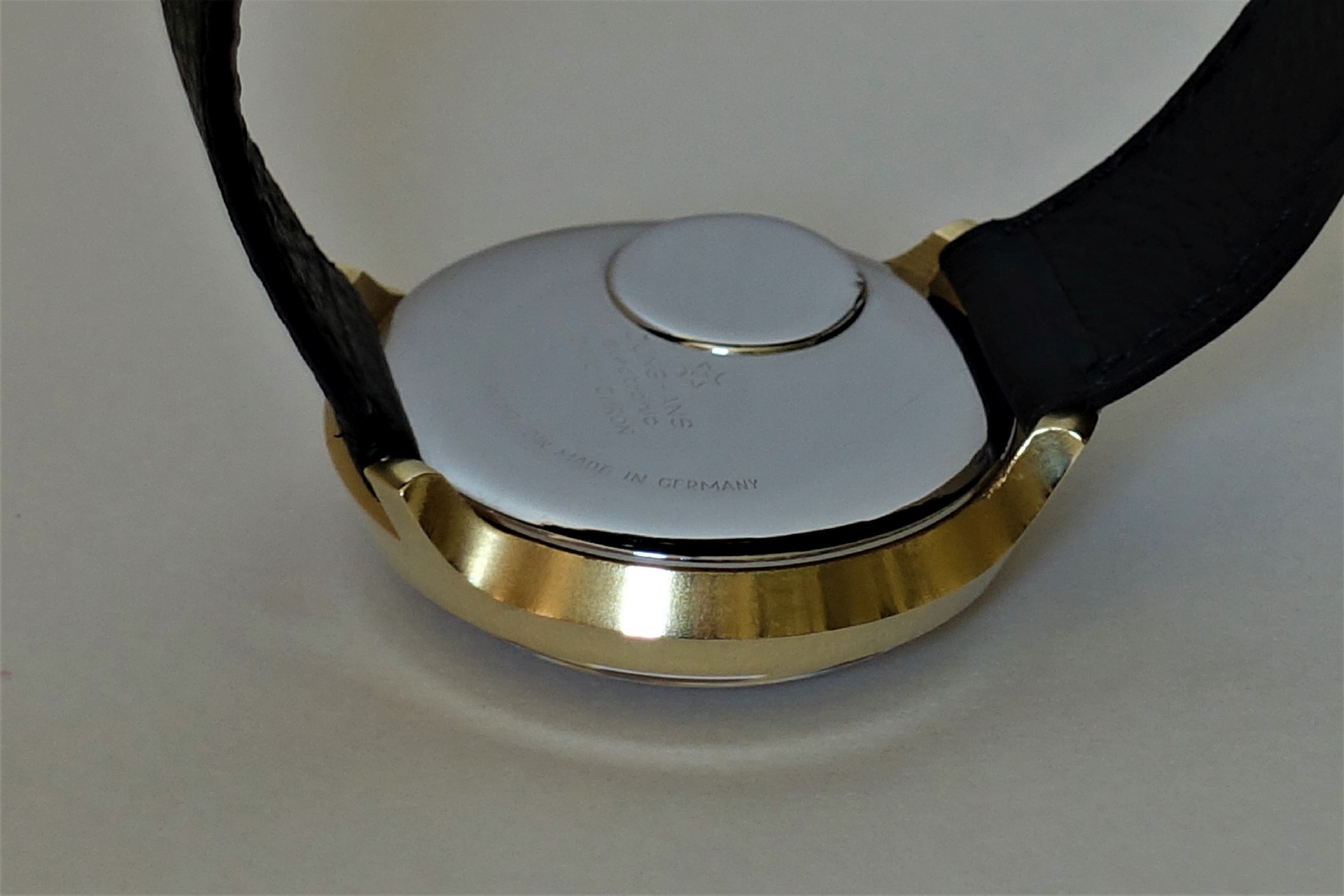 Silberfarbener Uhrenboden mit goldfarbenem Gehäuserand und schwarzem Armband.