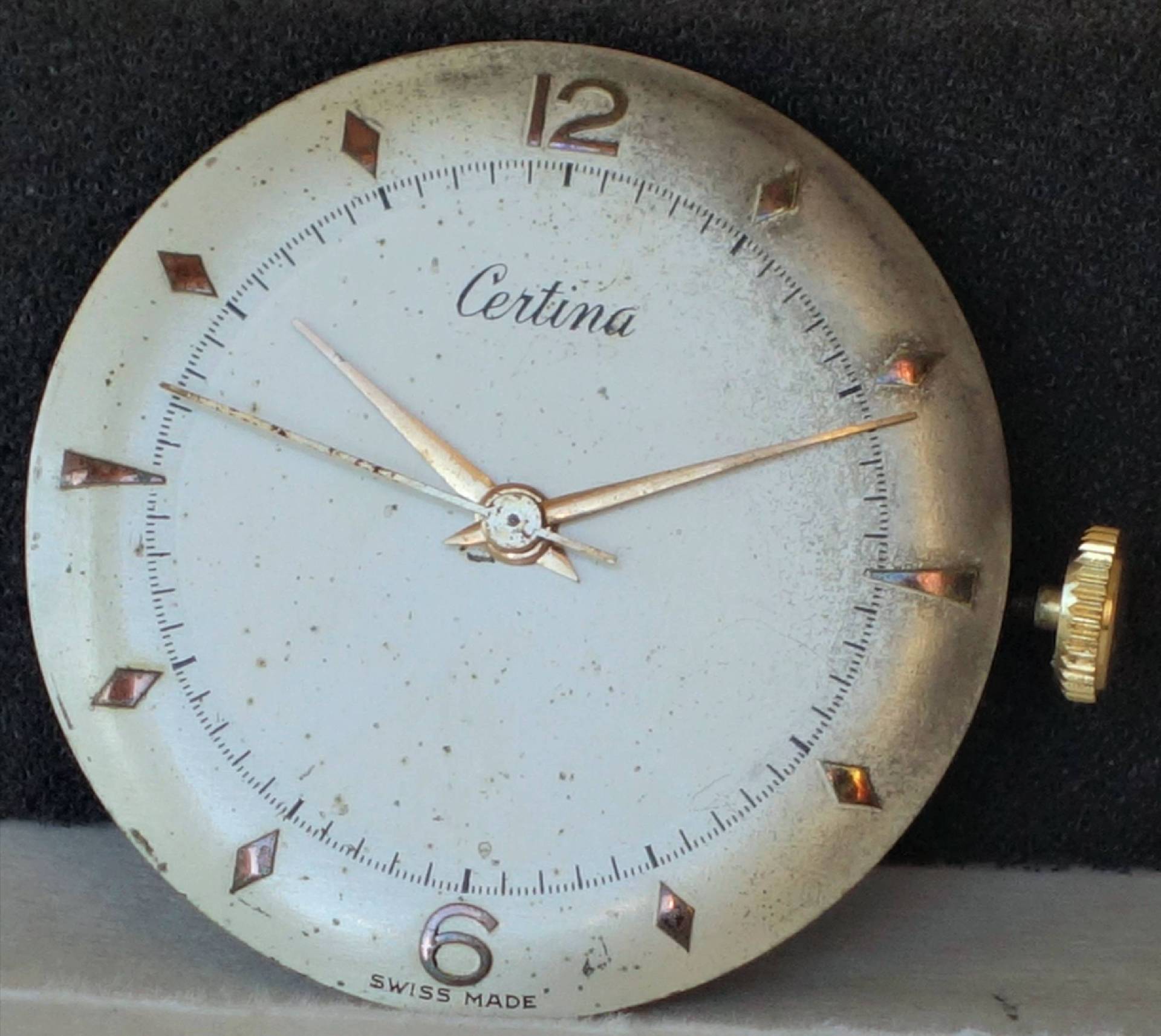 Rundes Uhrwerk mit weißem Zifferblatt, goldfarbenen Zeigern und Krone, Markierung "Certina" und "Swiss Made".