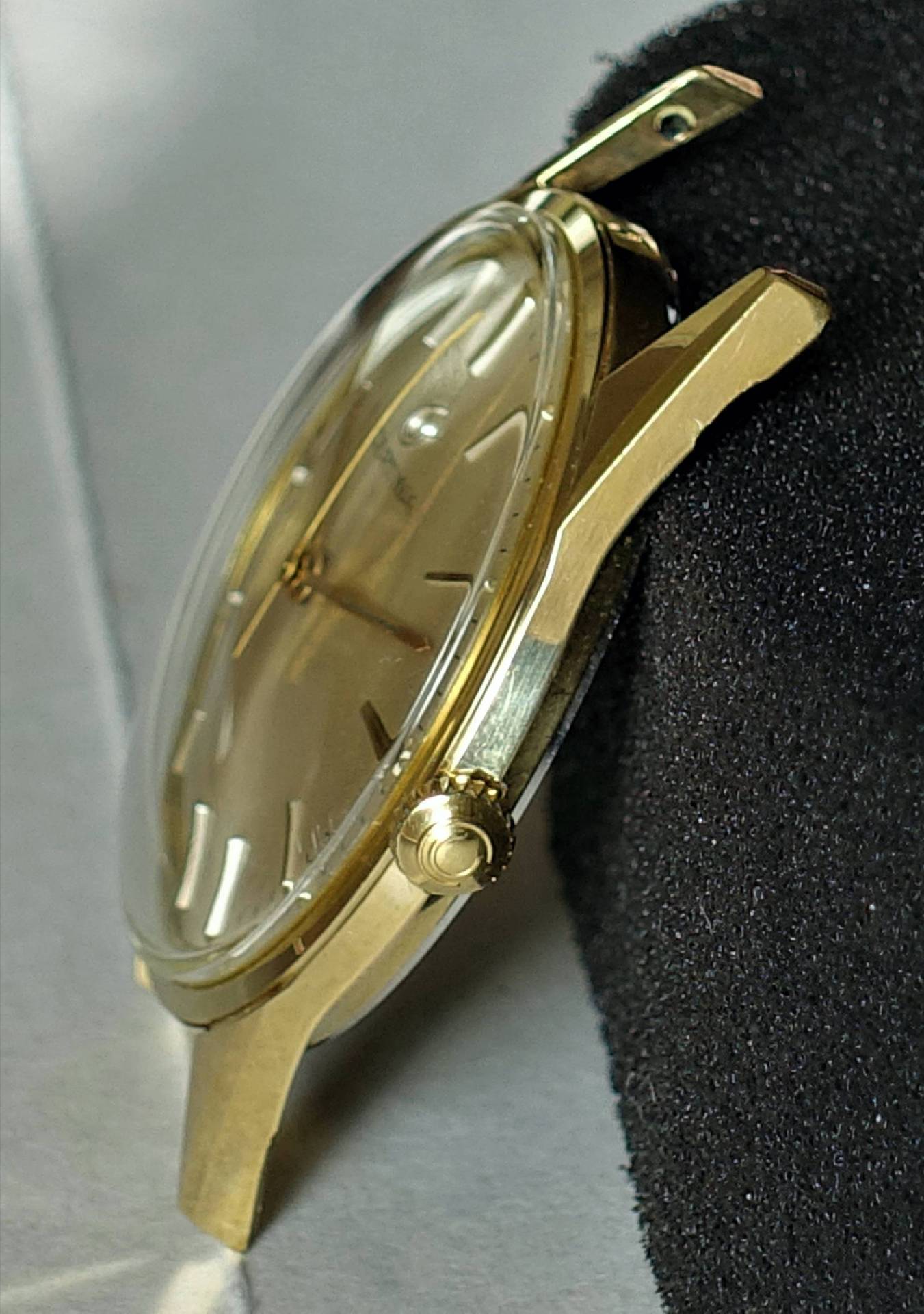 Goldfarbene Armbanduhr mit rundem Gehäuse und seitlicher Krone.