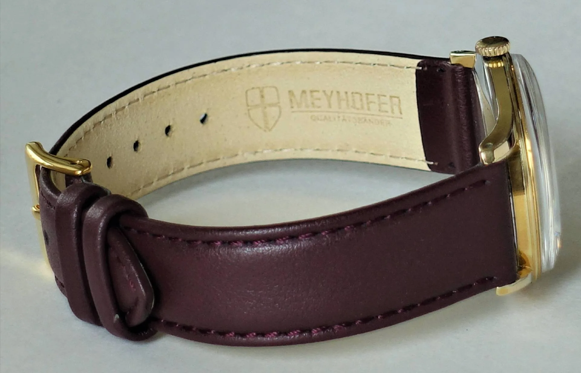 Braunes Uhrenarmband aus Leder mit goldfarbener Schließe.
