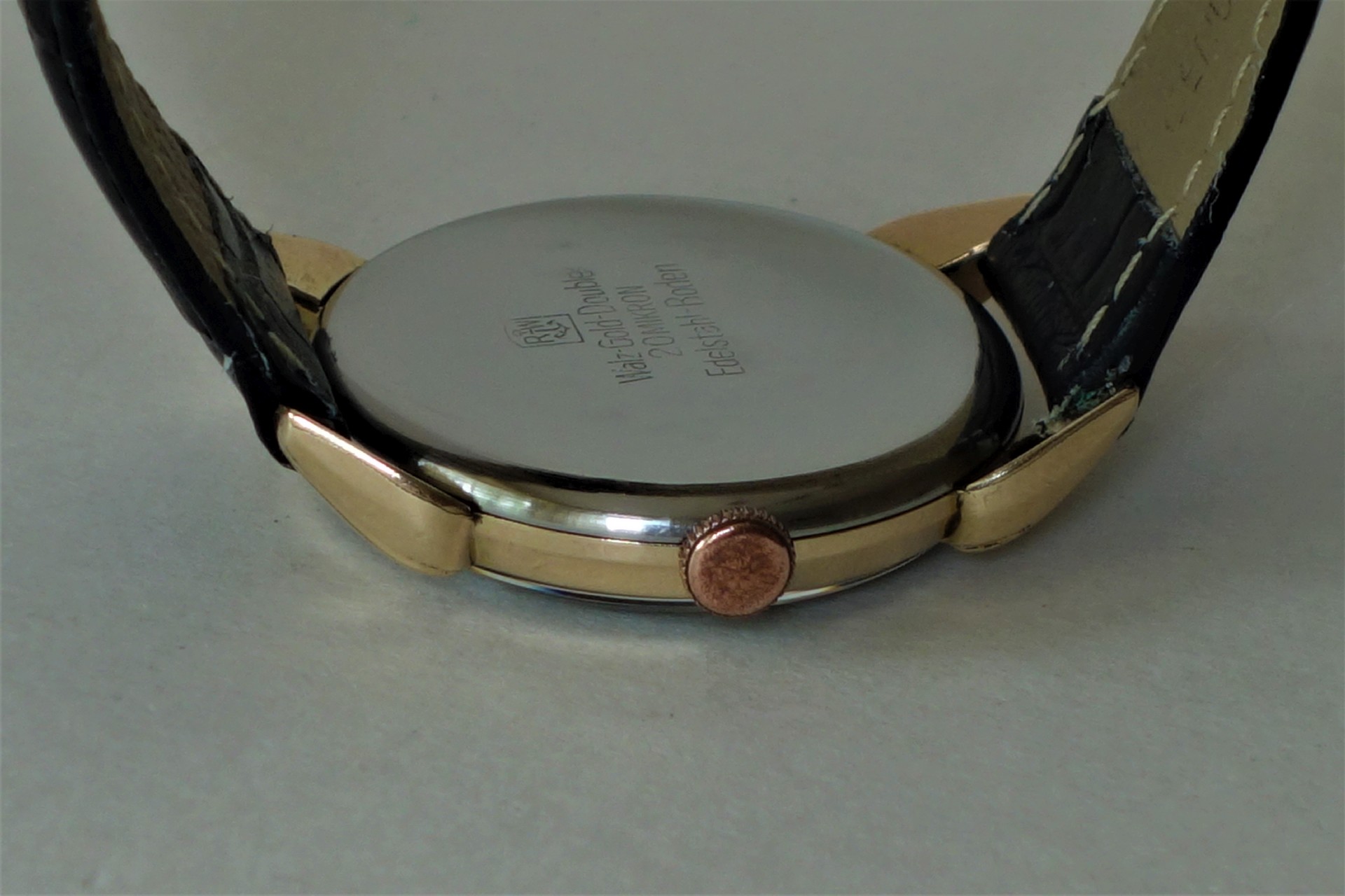Silberfarbener Uhrboden mit goldfarbenem Gehäuserand und schwarzem Armband.