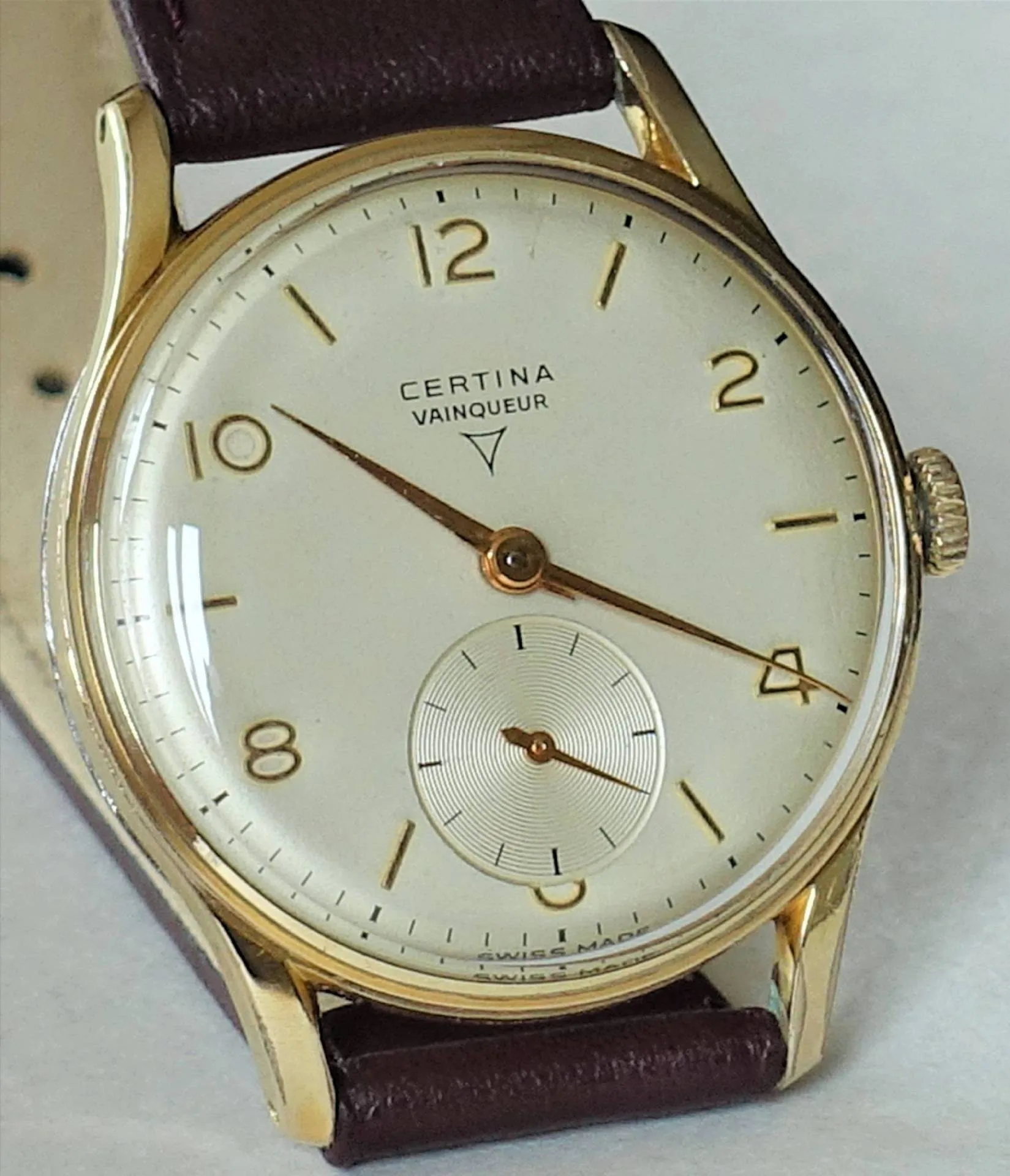 Certina Vainqueur Uhr Klassische Armbanduhr mit hellem Zifferblatt, goldfarbenem Gehäuse und braunem Armband.