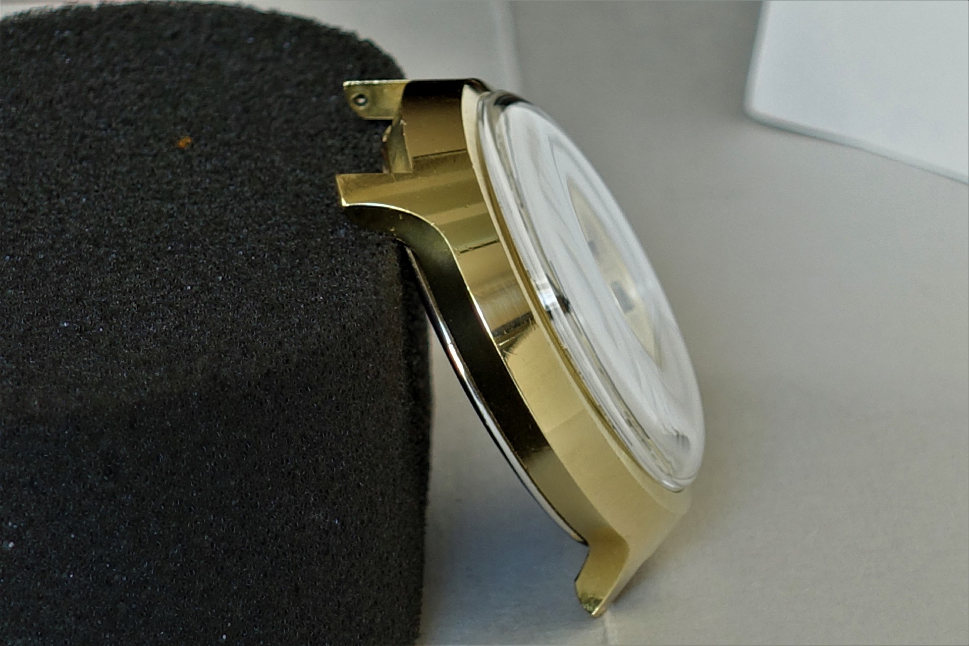 Goldfarbenes Uhrengehäuse mit montiertem Uhrglas, seitliche Ansicht.