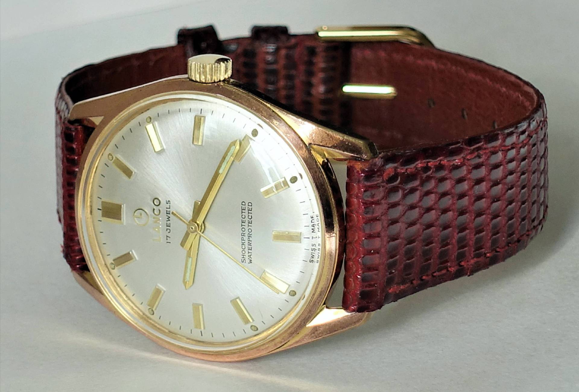 Goldfarbene Armbanduhr mit silbernem Zifferblatt und braunem Armband.