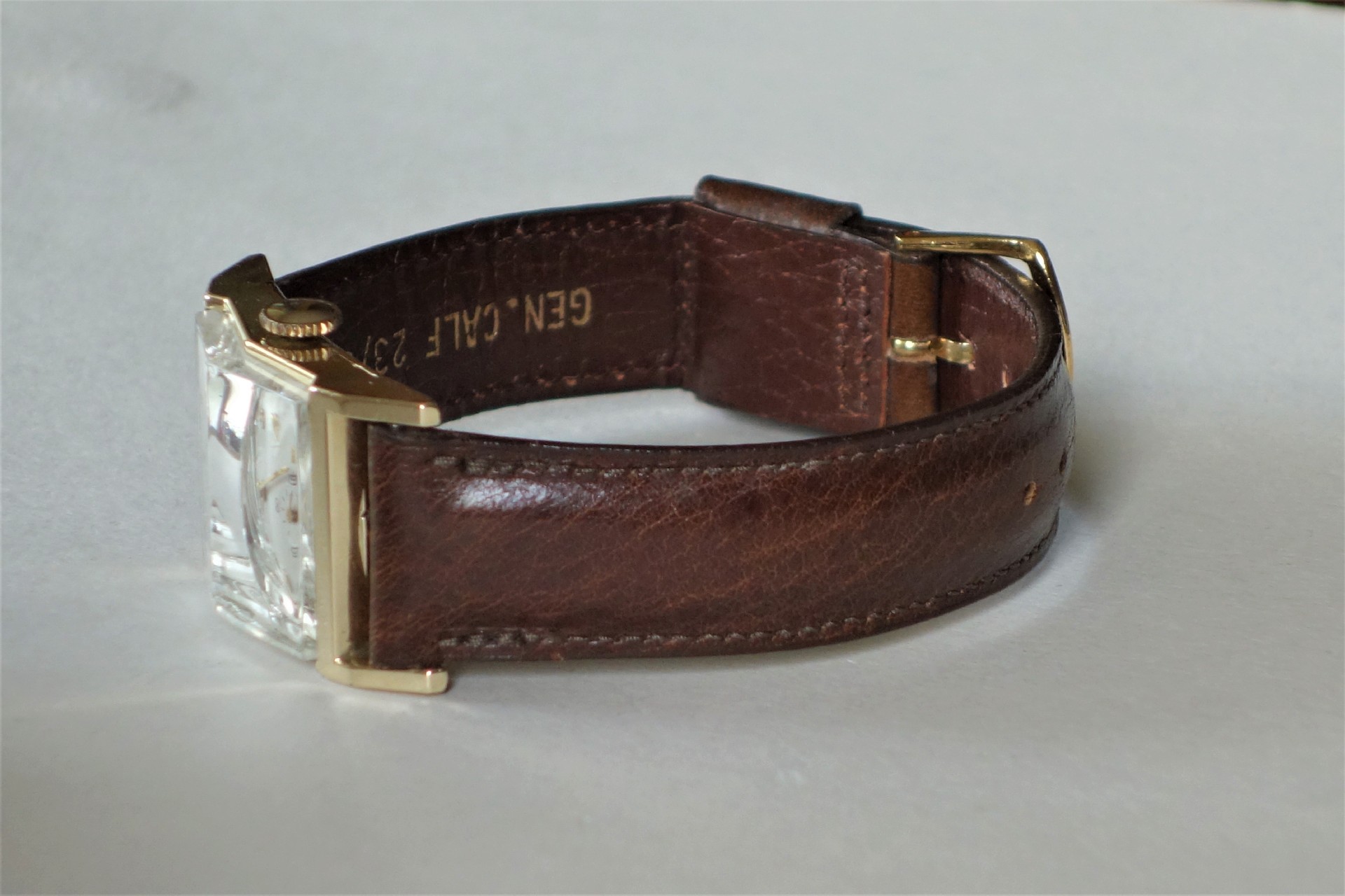 Armbanduhr mit braunem Lederarmband und rechteckigem Gehäuse in goldfarbener Optik.