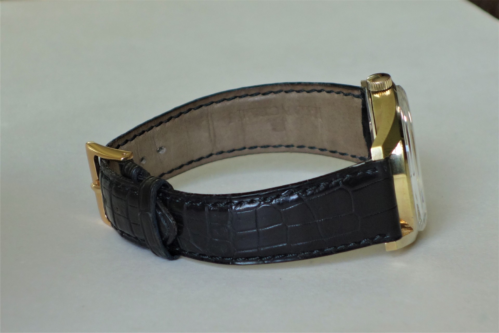 Armbanduhr mit schwarzem Lederarmband in Krokodiloptik und goldfarbenem Gehäuse.