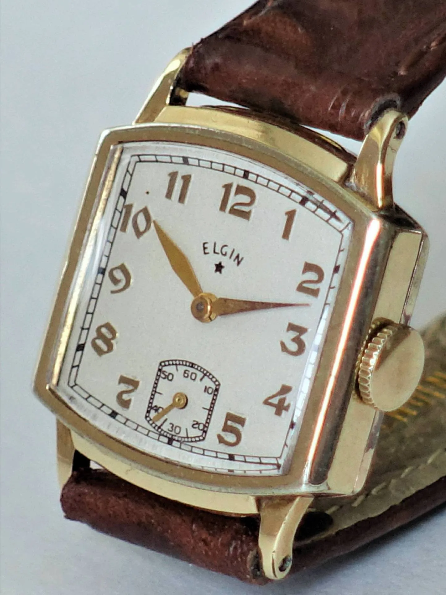 Rechteckige goldfarbene Vintage-Uhr Eine rechteckige, goldfarbene Armbanduhr mit braunem Lederarmband und kleiner Sekunde auf dem Zifferblatt.