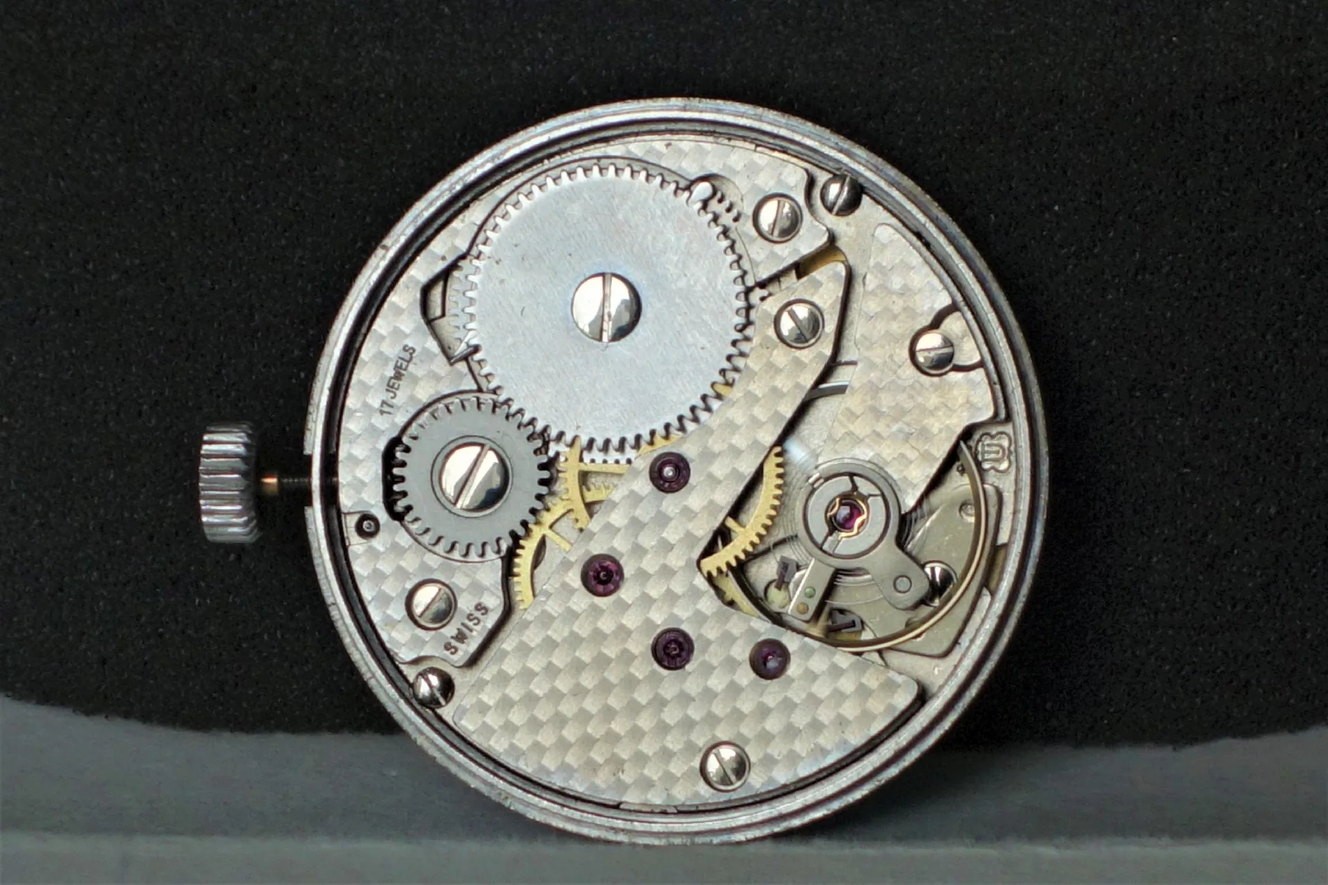 Mechanisches Uhrwerk in silberner Farbe mit sichtbaren Zahnrädern und Aufzugskrone.