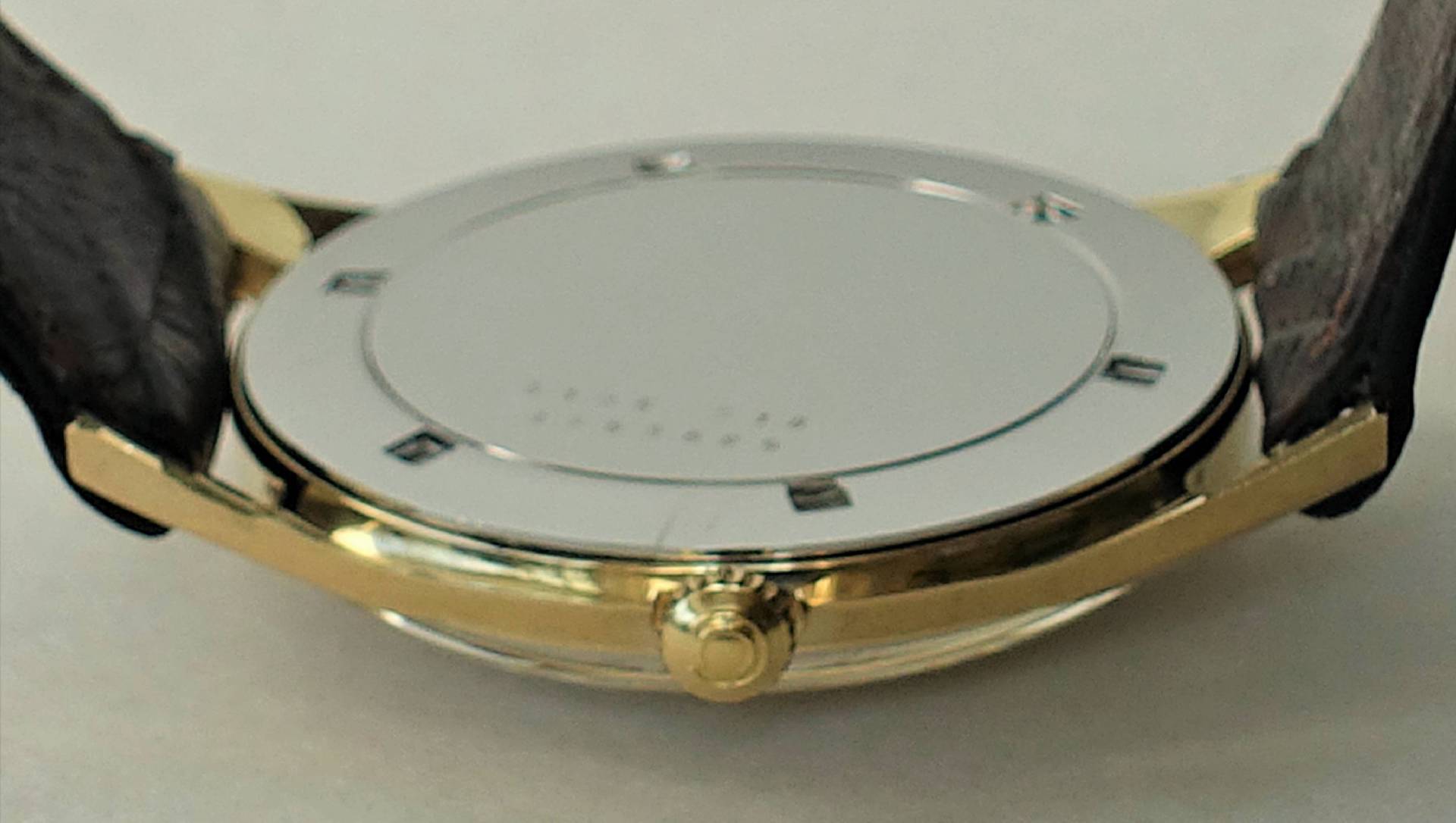 Silberfarbener Boden einer Armbanduhr mit goldfarbenem Gehäuserand und schwarzem Armband.