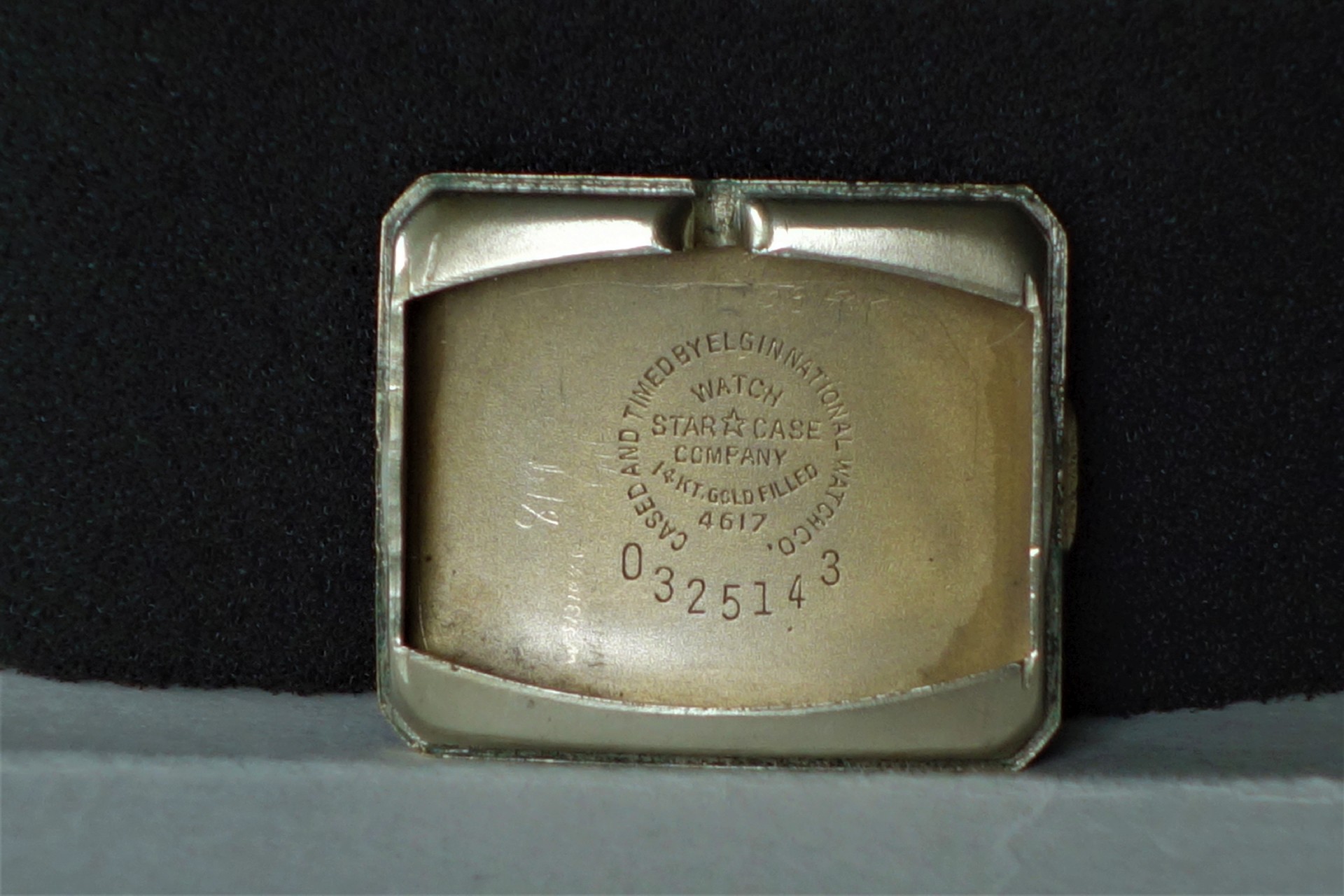 Rechteckiger goldfarbener Gehäuseboden für Armbanduhr mit Gravur und Seriennummer.