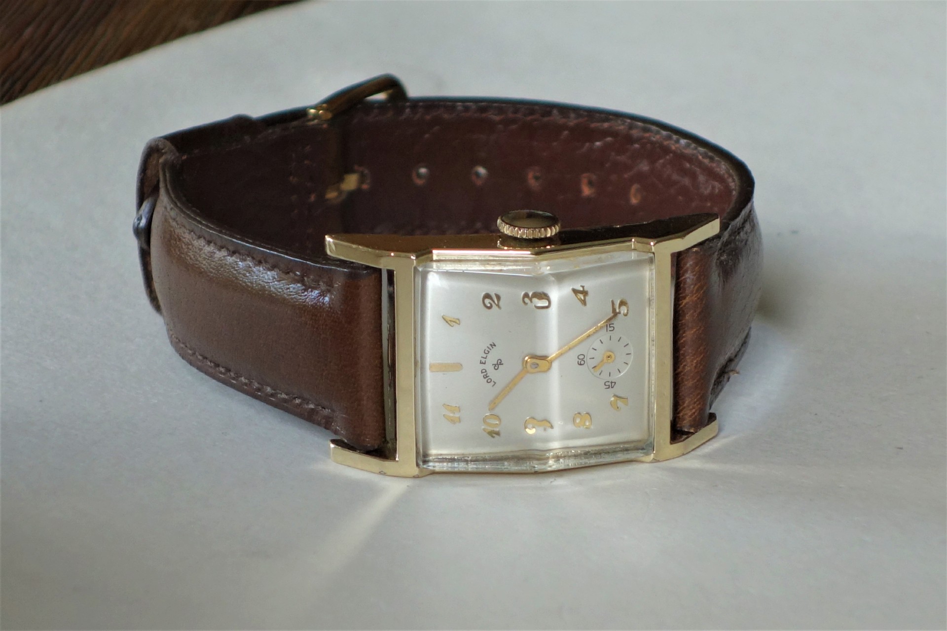Rechteckige Armbanduhr mit braunem Armband und hellem Zifferblatt.