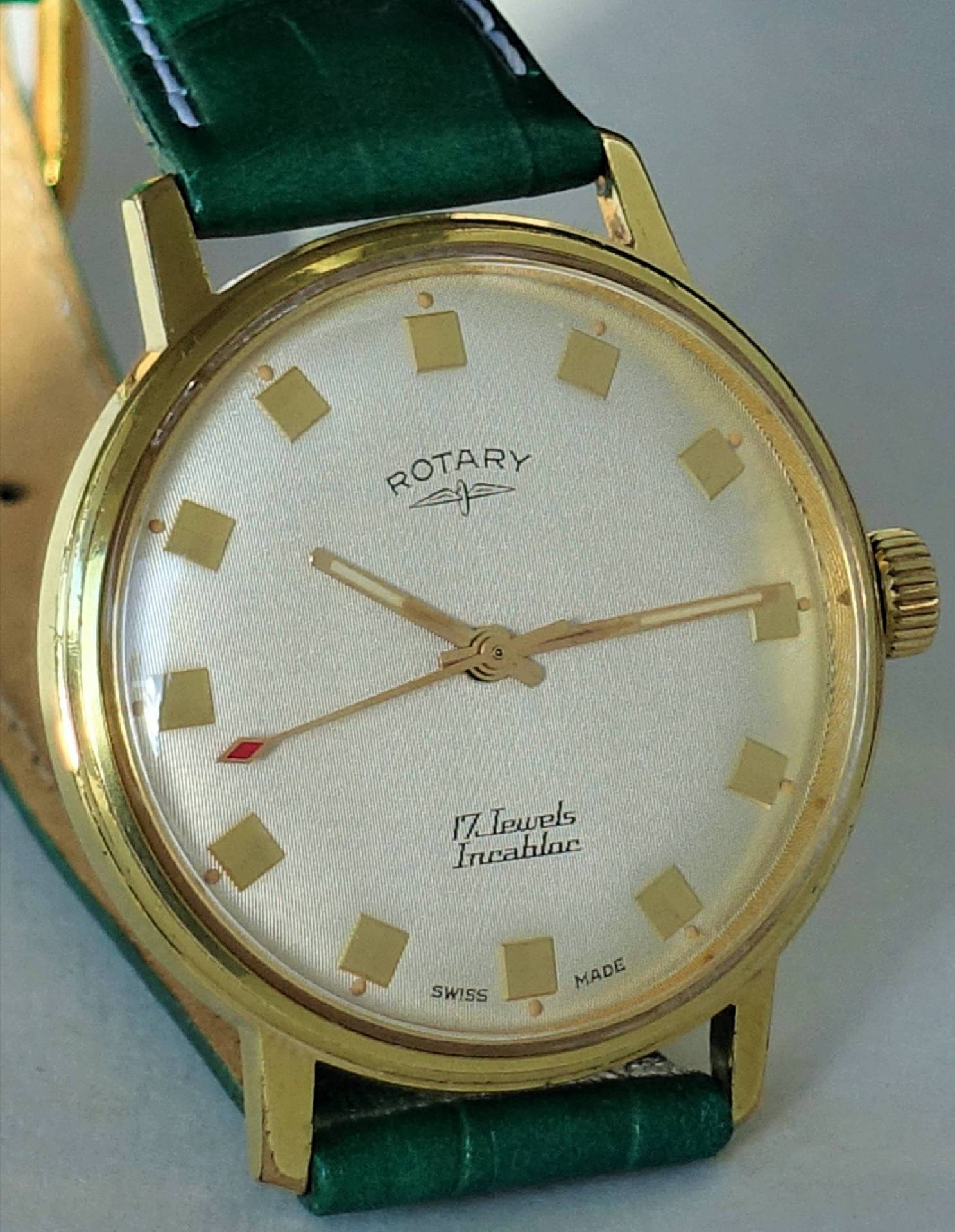 Goldfarbene Armbanduhr mit grünem Armband und hellem Zifferblatt.