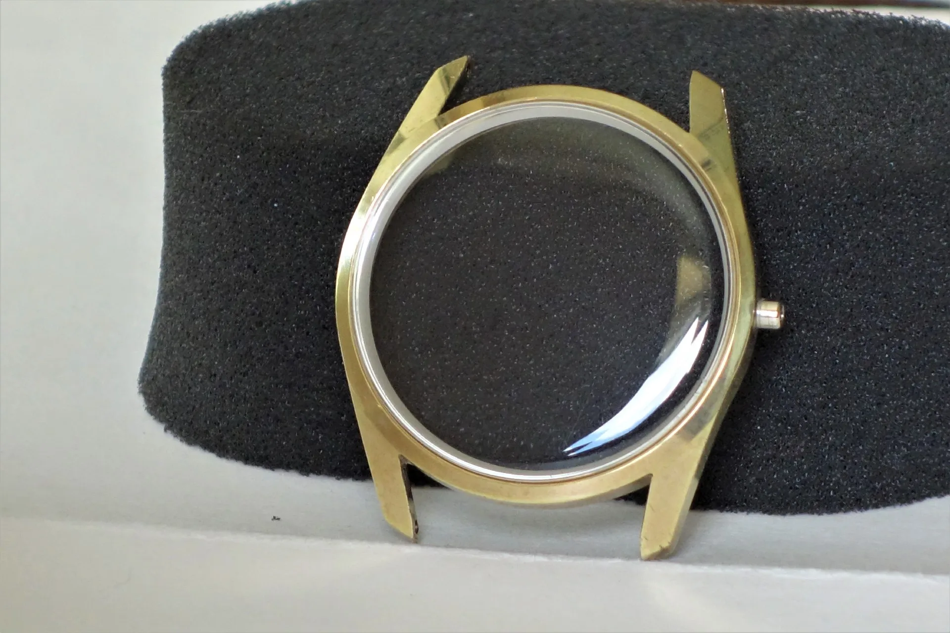 Rundes Uhrgehäuse aus goldfarbenem Metall mit montiertem Uhrglas, ohne Uhrwerk und Armband.