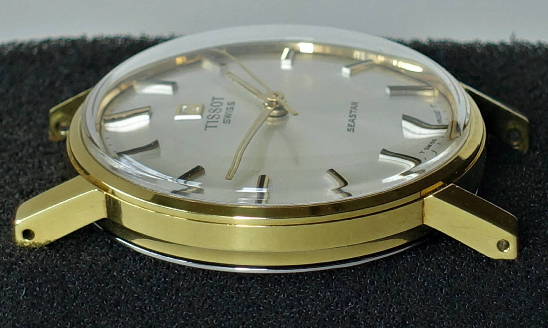 Flache Armbanduhr mit goldfarbenem Gehäuse und hellem Zifferblatt.