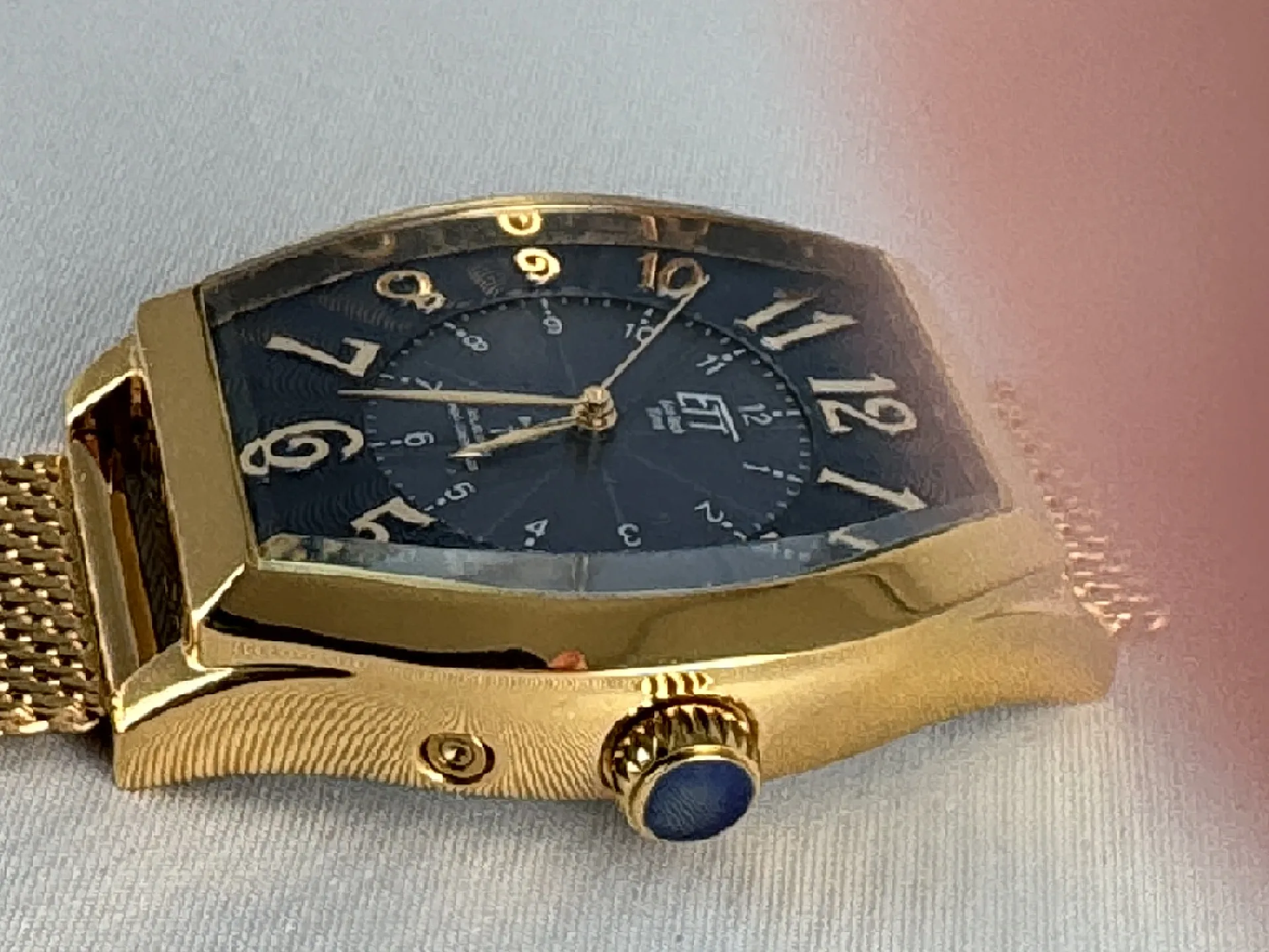Goldfarbene Armbanduhr mit schwarzem Zifferblatt und Mesh-Armband in Tonneauform.