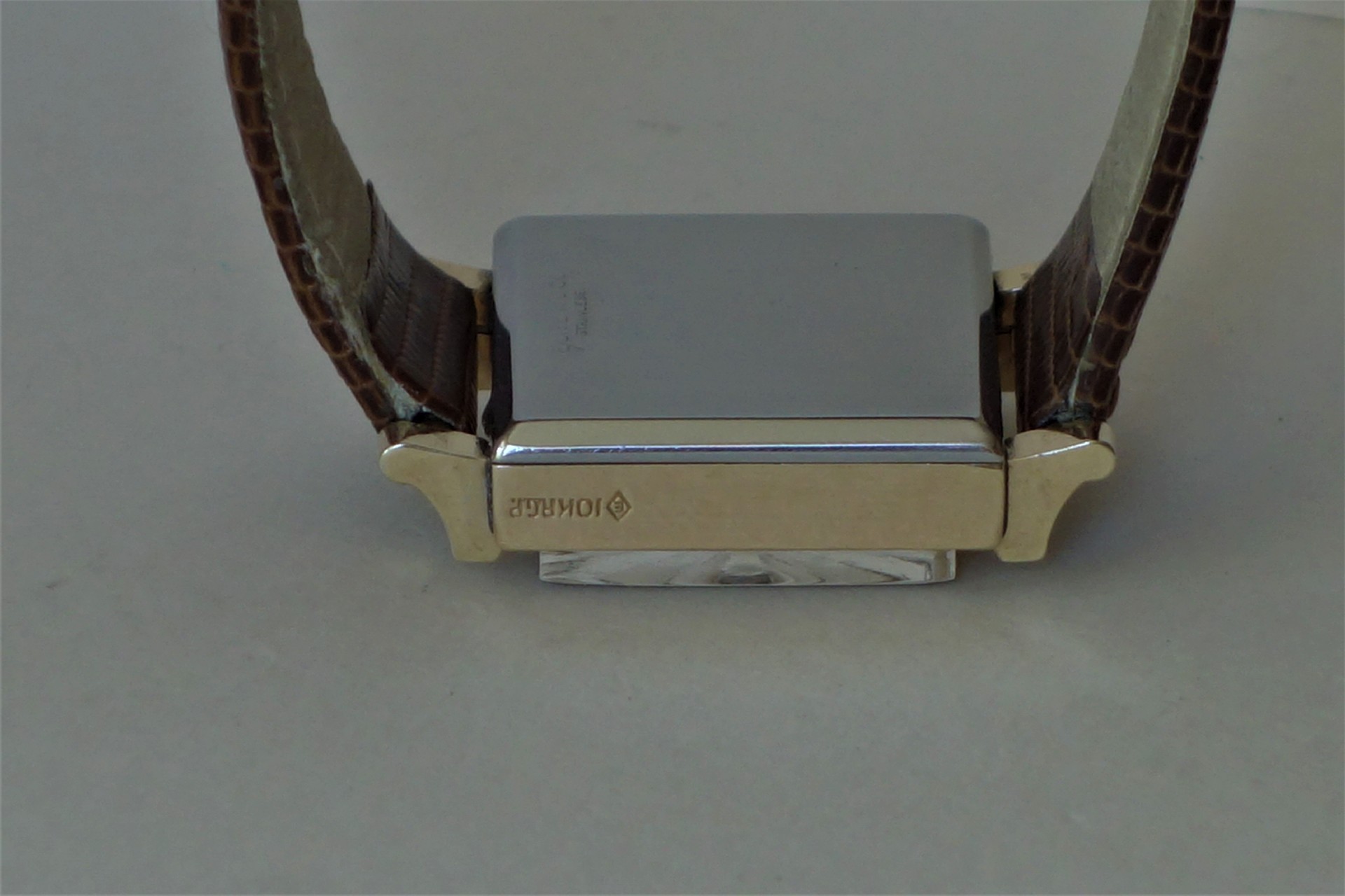 Rechteckige Armbanduhr mit braunem Lederarmband und Metallgehäuse, Rückseite sichtbar.