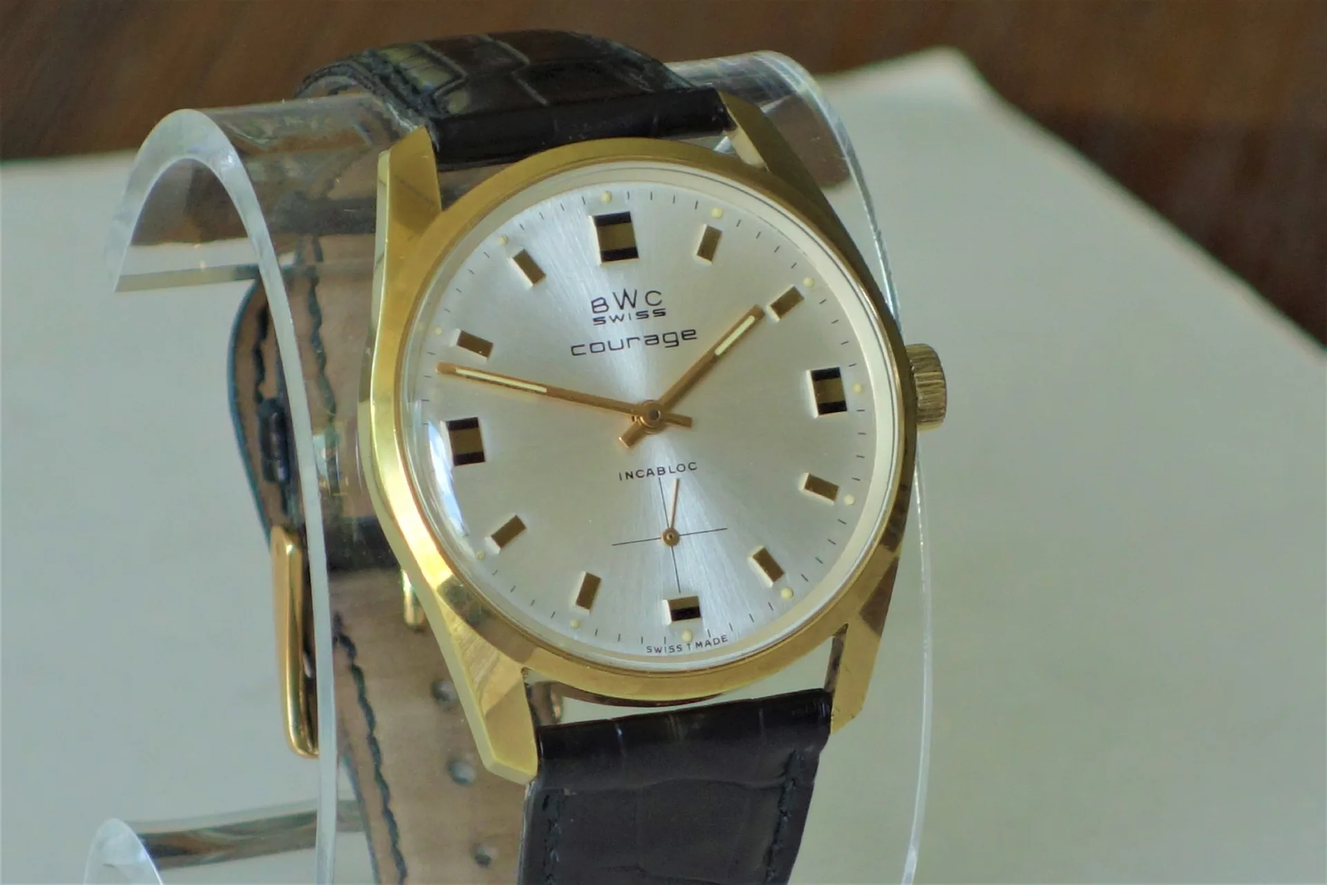 BWC Swiss Armbanduhr goldfarben Goldfarbene Armbanduhr mit silbernem Zifferblatt und schwarzem Lederarmband.