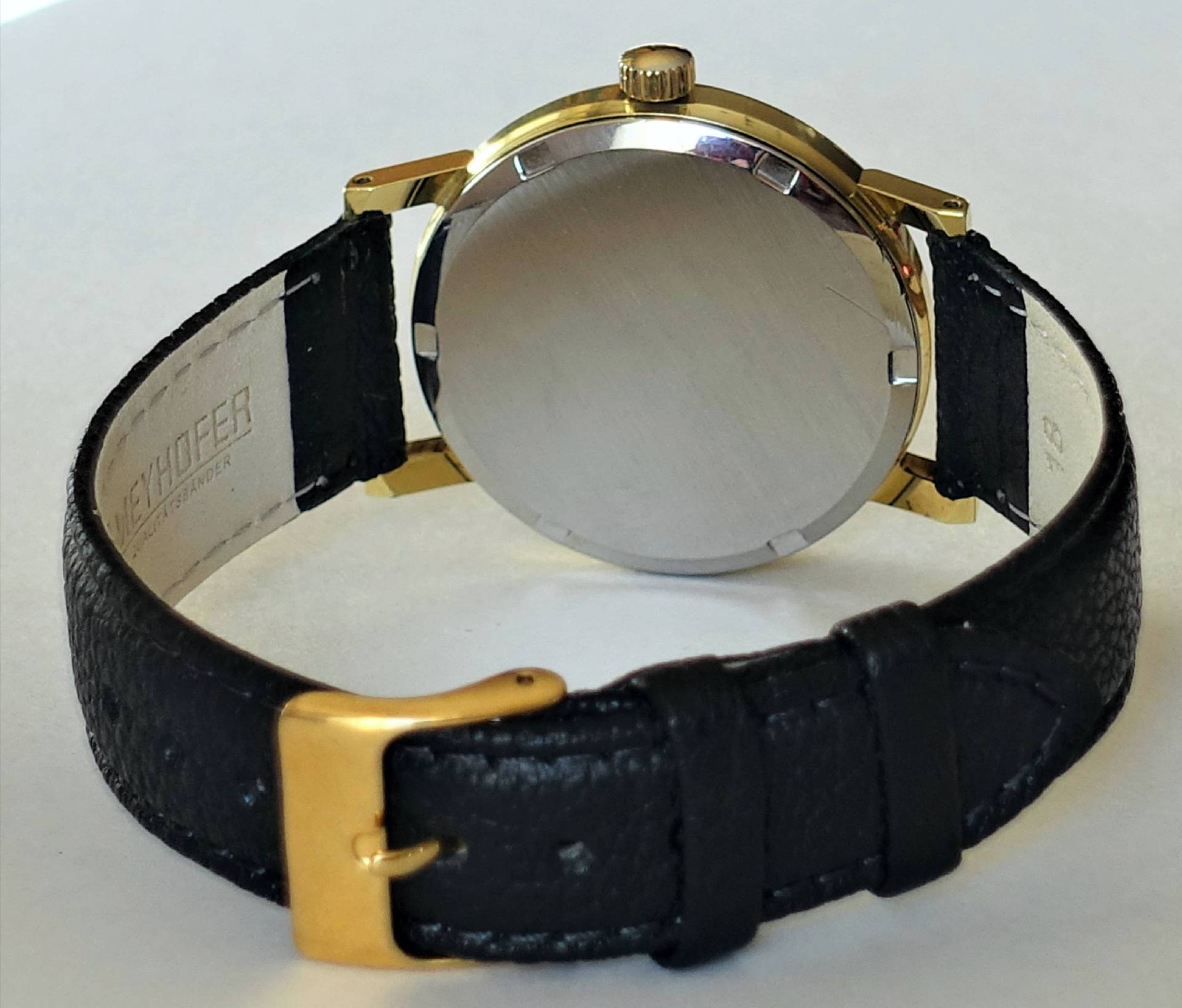 Schwarze Armbanduhr mit goldfarbenem Gehäuse und Schließe, Rückseite sichtbar.