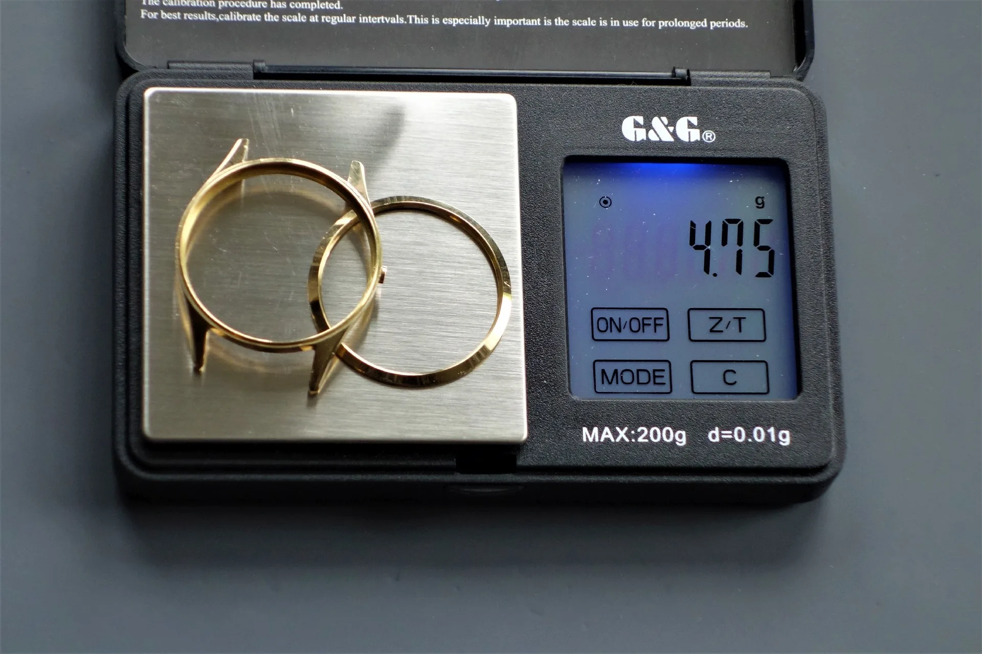 Uhrengehäuse goldfarben Zwei goldfarbene Uhrengehäuse ohne Uhrwerk auf einer digitalen Waage.