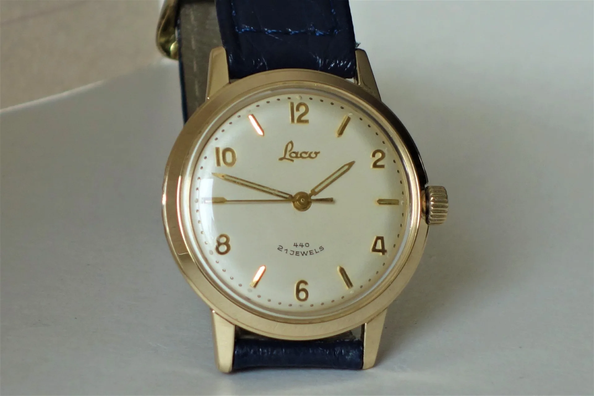 Analoge Armbanduhr mit goldfarbenem Gehäuse, hellem Zifferblatt und dunkelblauem Armband.