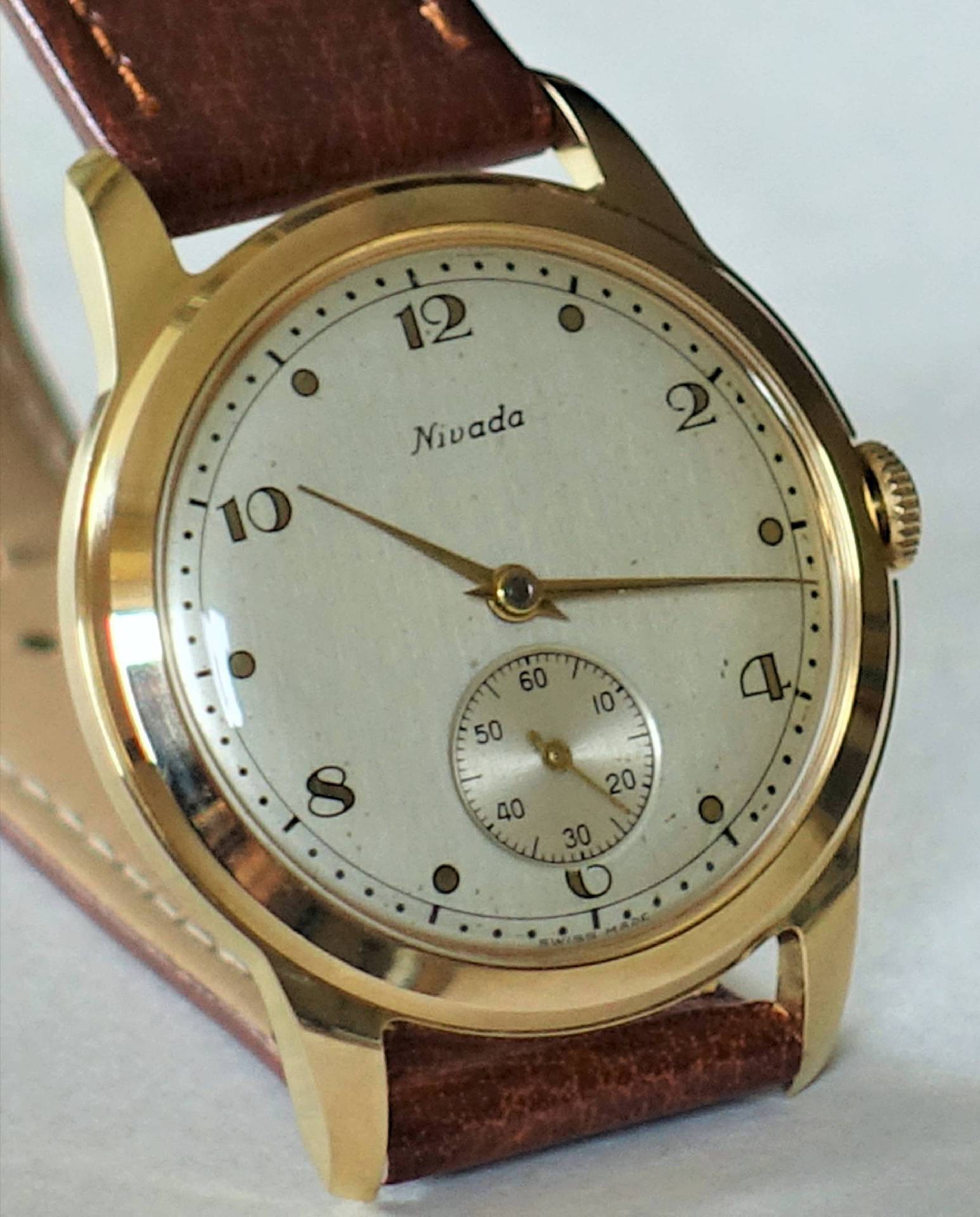 Goldfarbene Armbanduhr mit weißem Zifferblatt und braunem Armband.