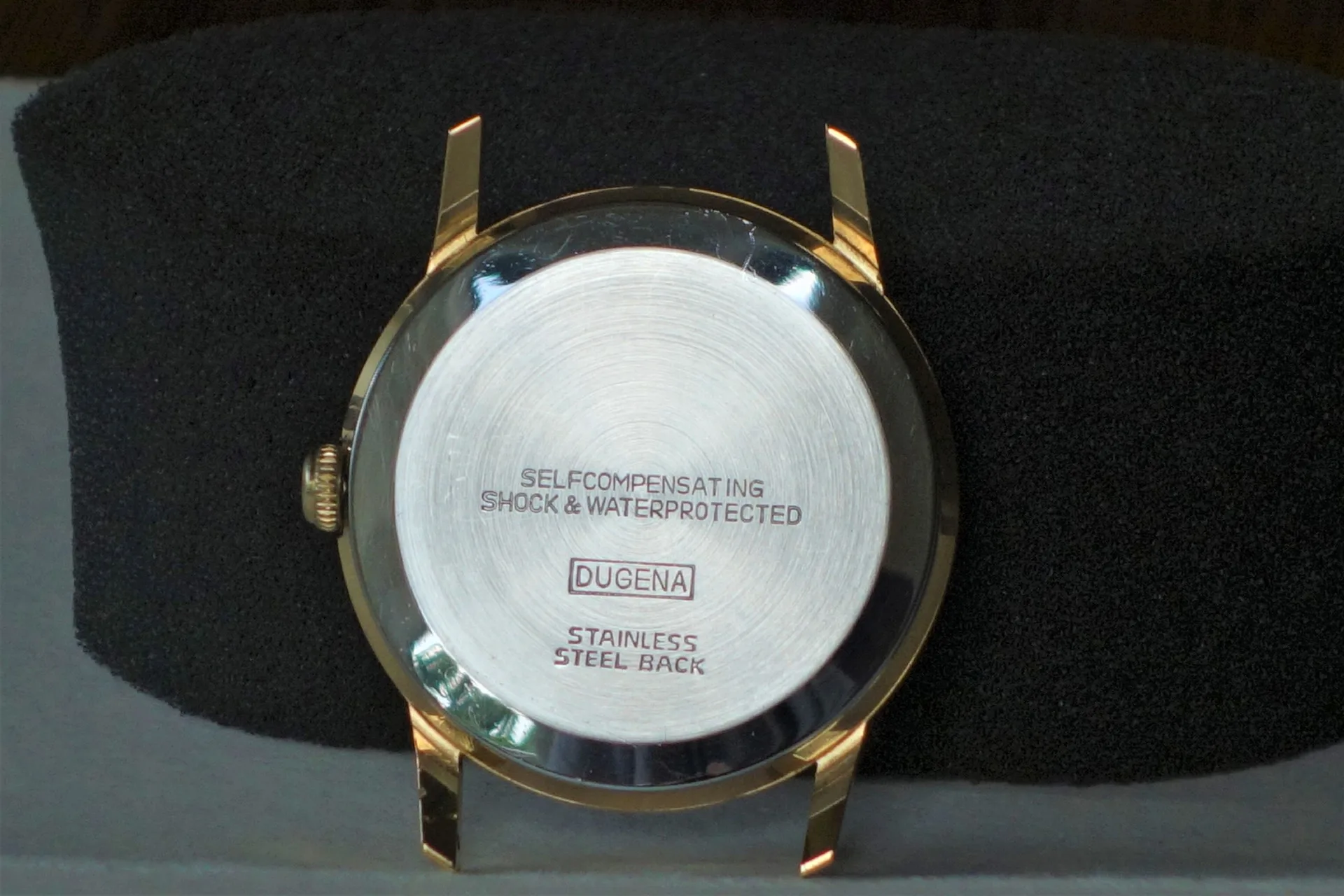 Dugena Uhrengehäuse Rückseite Rückseite eines goldfarbenen Uhrengehäuses mit silbernem Boden und Dugena Gravur.