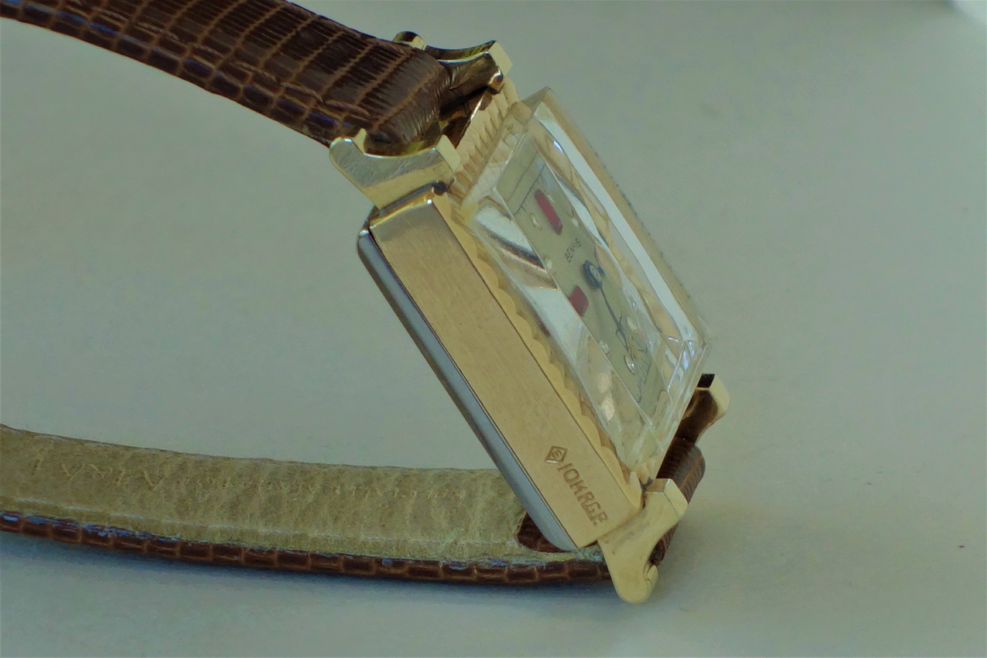 Rechteckige Armbanduhr mit goldfarbenem Gehäuse und braunem Lederarmband.