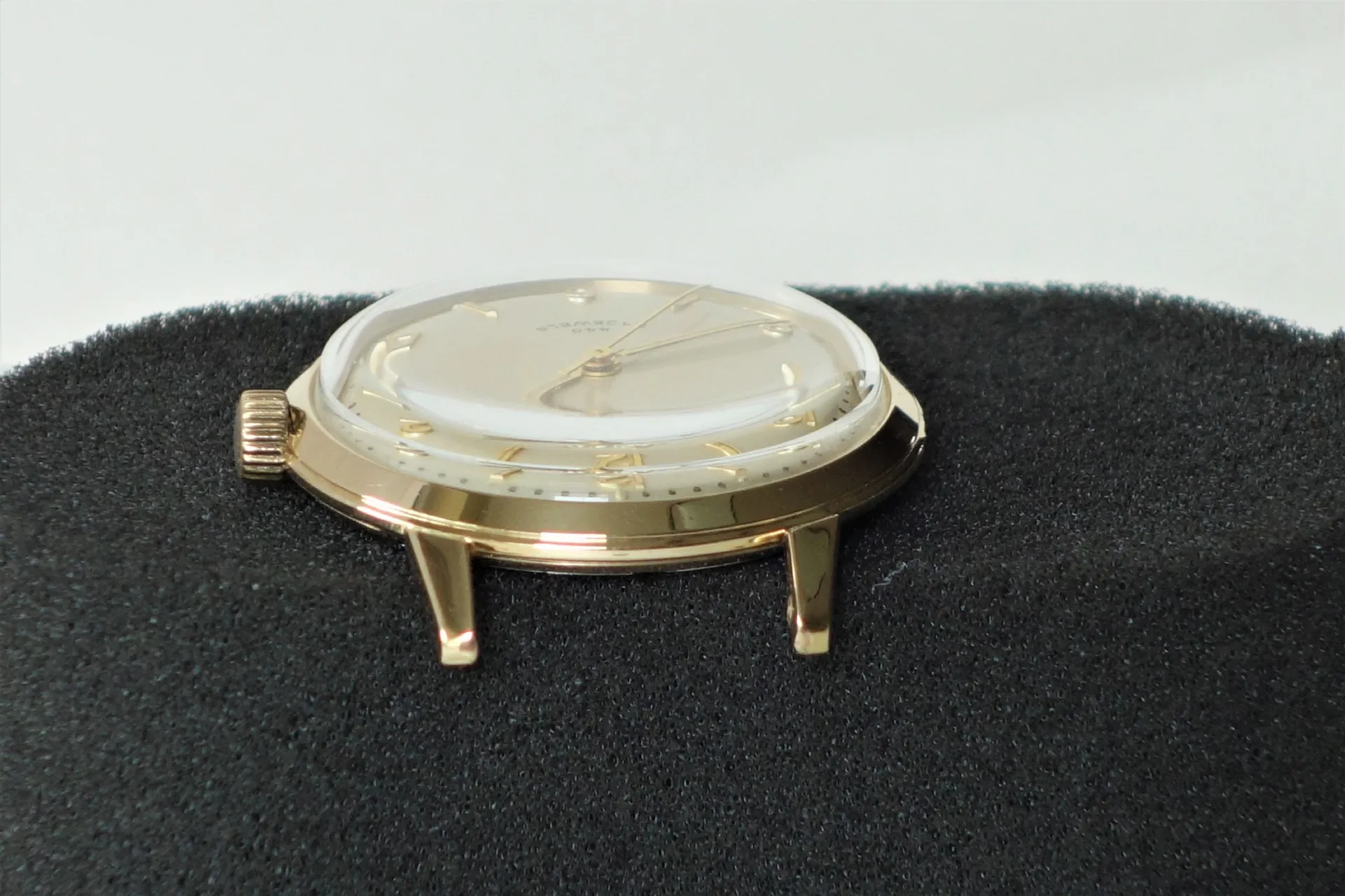 Goldfarbenes Uhrgehäuse mit Zifferblatt, Zeigern und Krone ohne Armband.