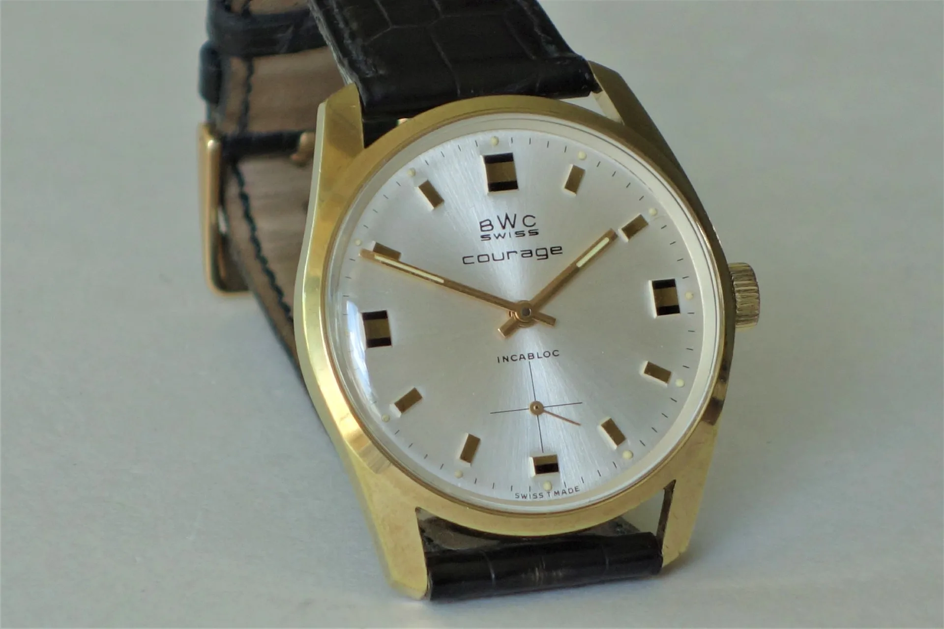 Analoge Armbanduhr mit goldfarbenem Gehäuse, silbernem Zifferblatt und schwarzem Lederarmband.
