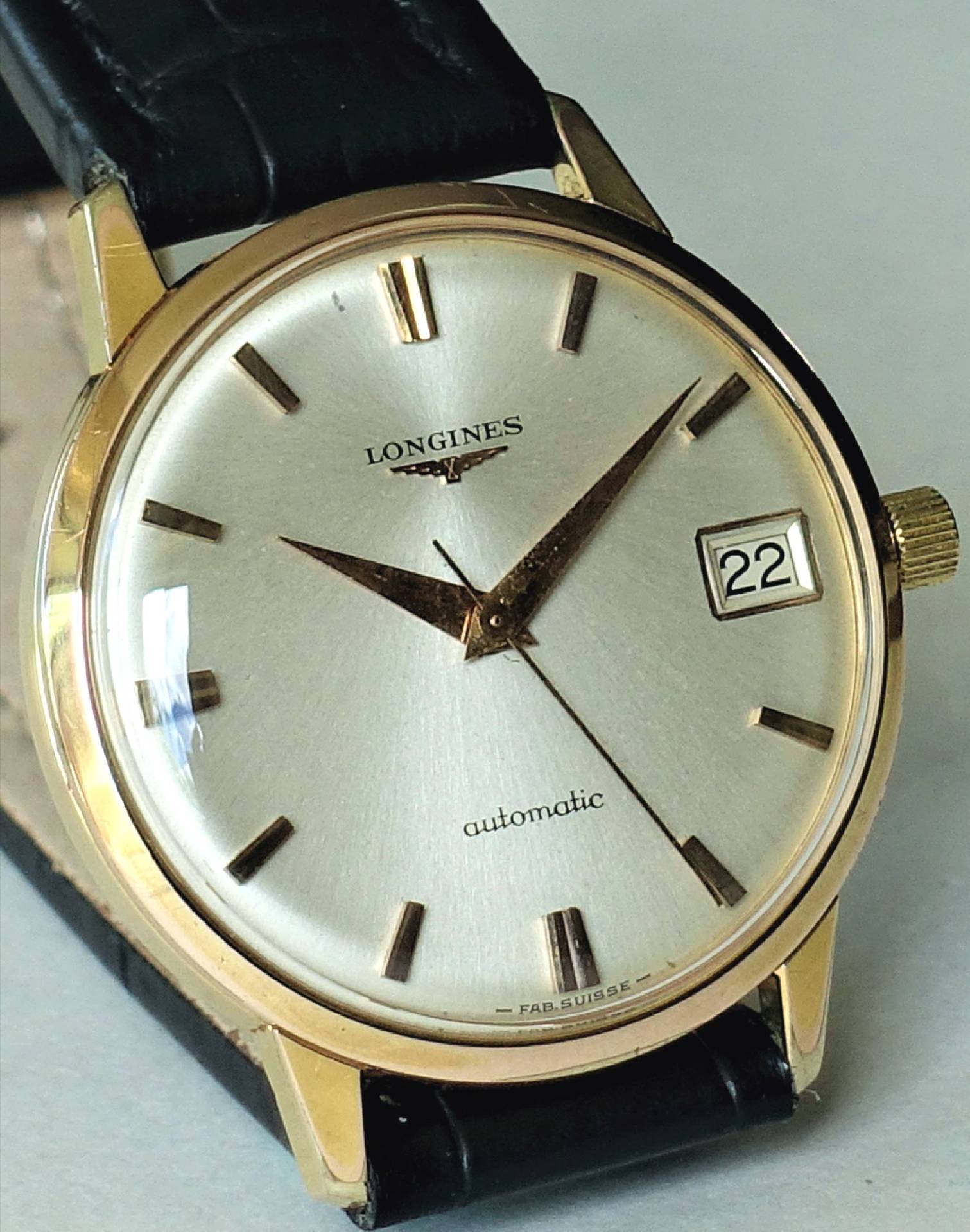 Goldfarbene Armbanduhr mit silbernem Zifferblatt, schwarzem Armband und Datumsanzeige.