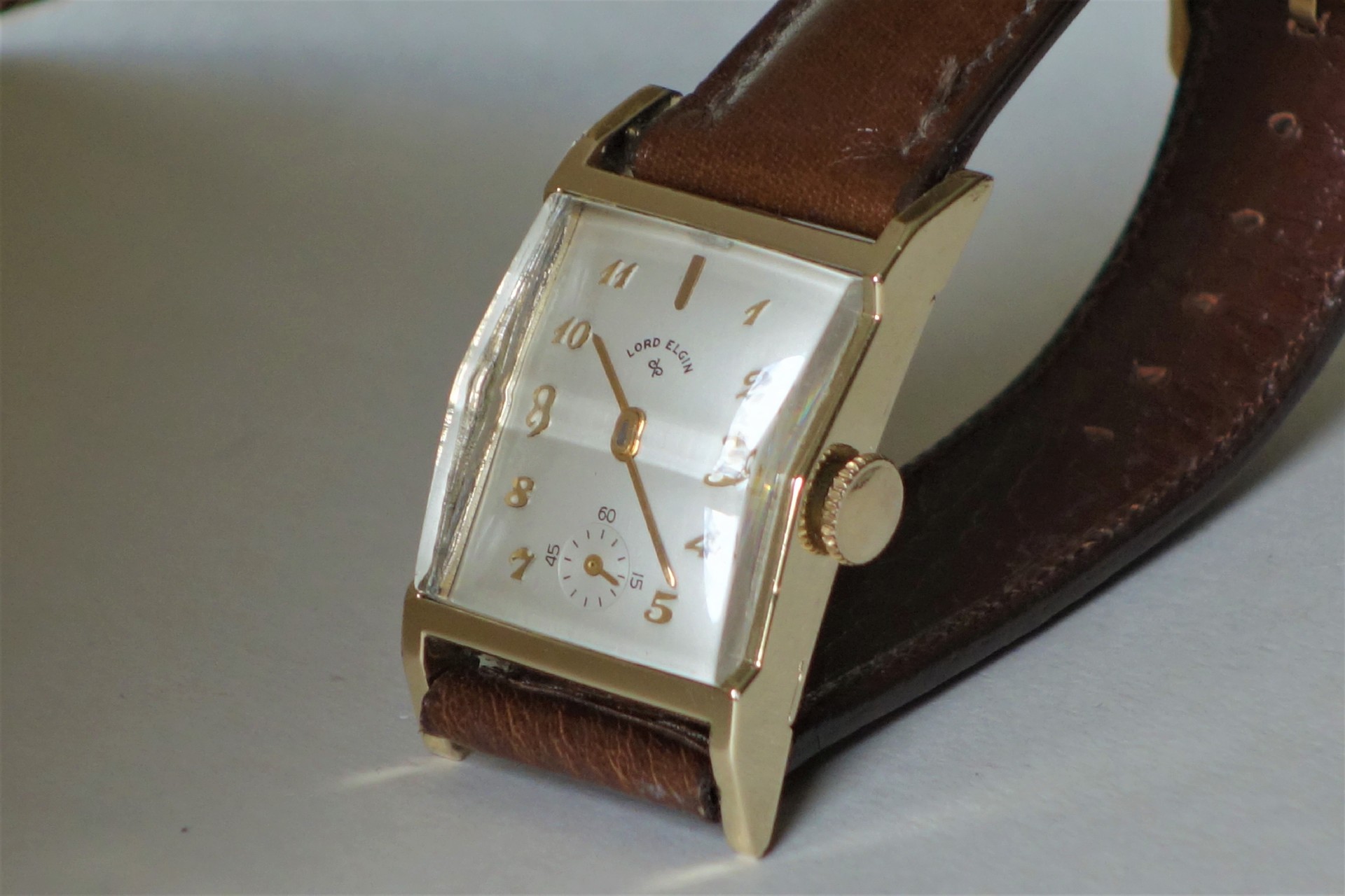 Rechteckige Armbanduhr mit braunem Armband und hellem Zifferblatt.