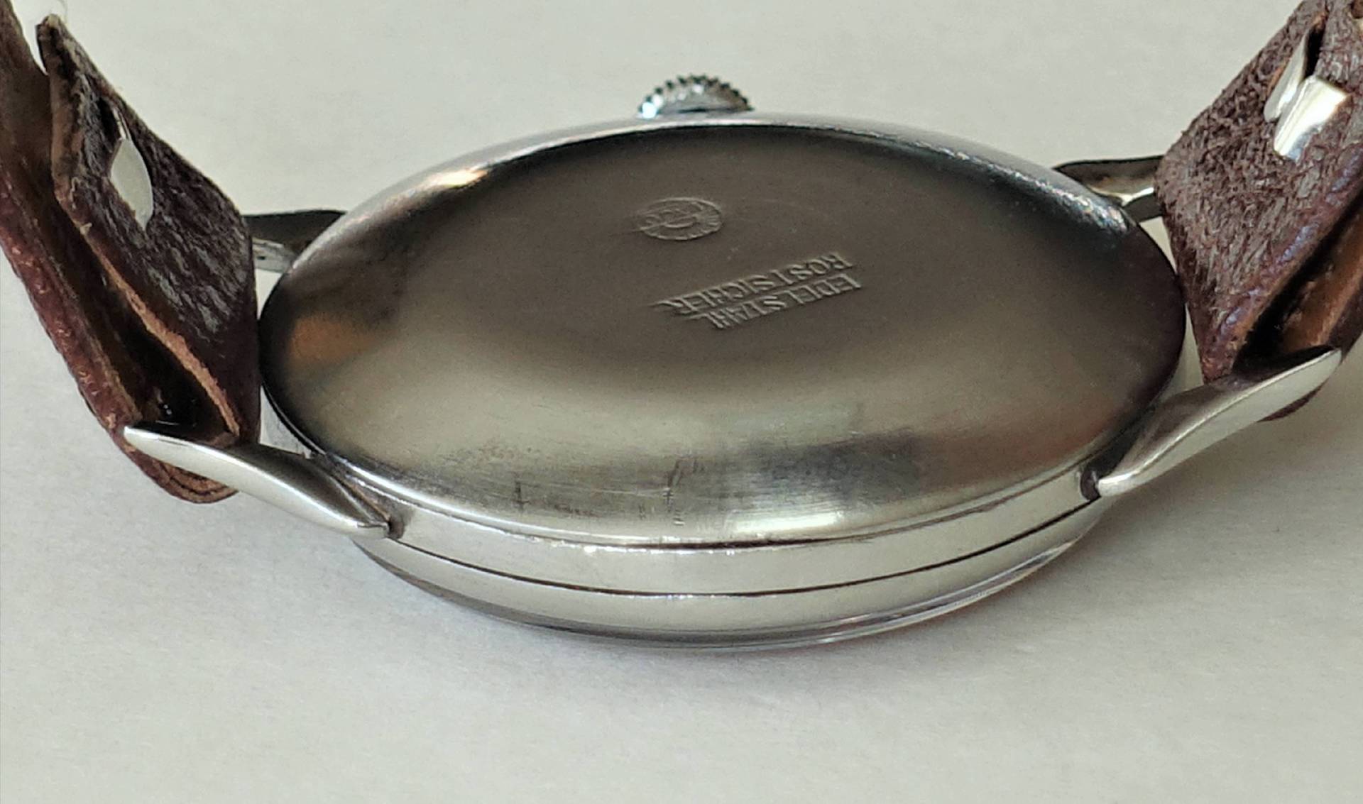 Runder Uhrenboden aus silberfarbenem Edelstahl mit braunem Lederarmband.