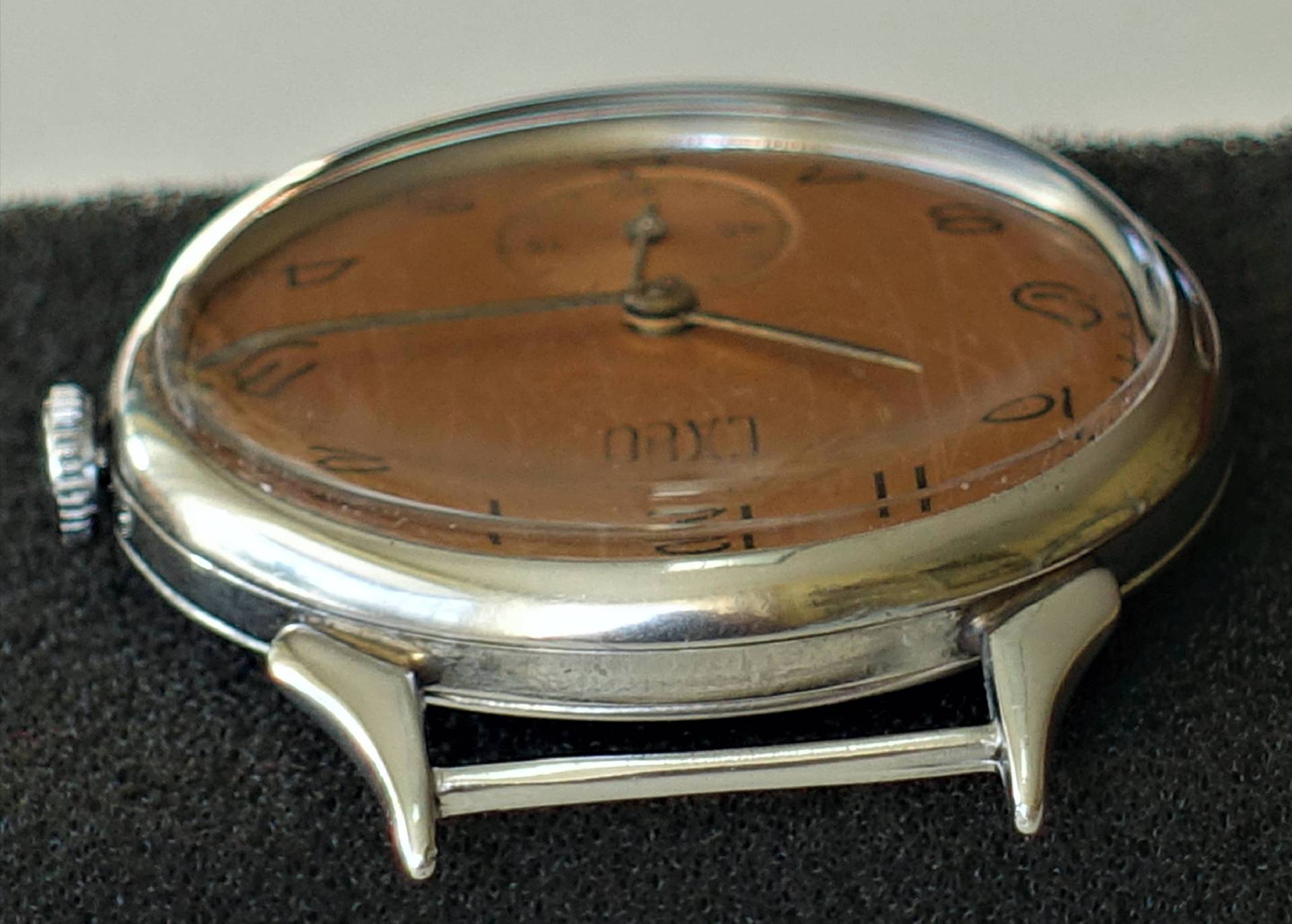 Flache Armbanduhr mit braunem Zifferblatt und silberfarbenem Gehäuse.