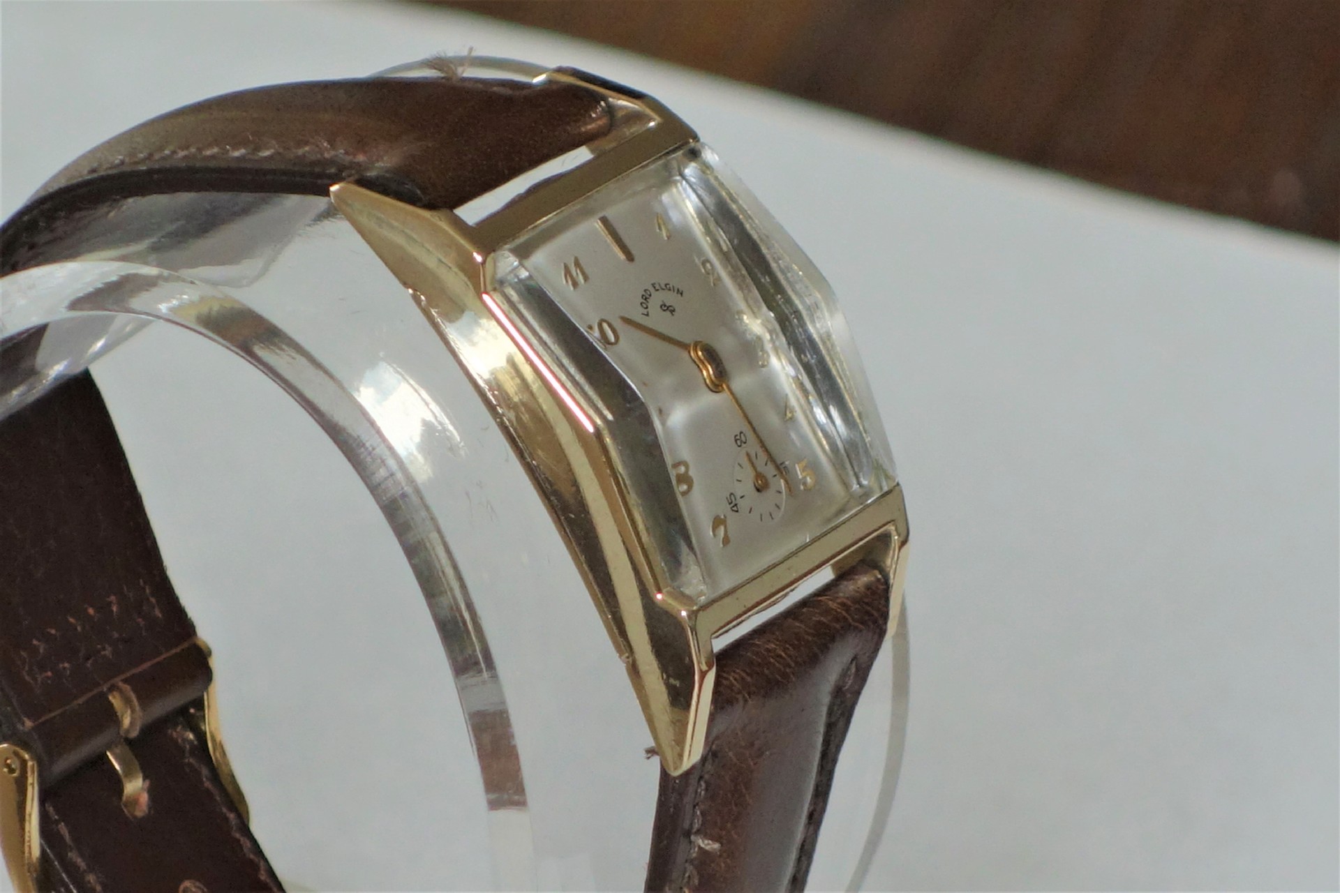 Rechteckige Armbanduhr mit braunem Armband und hellem Zifferblatt.