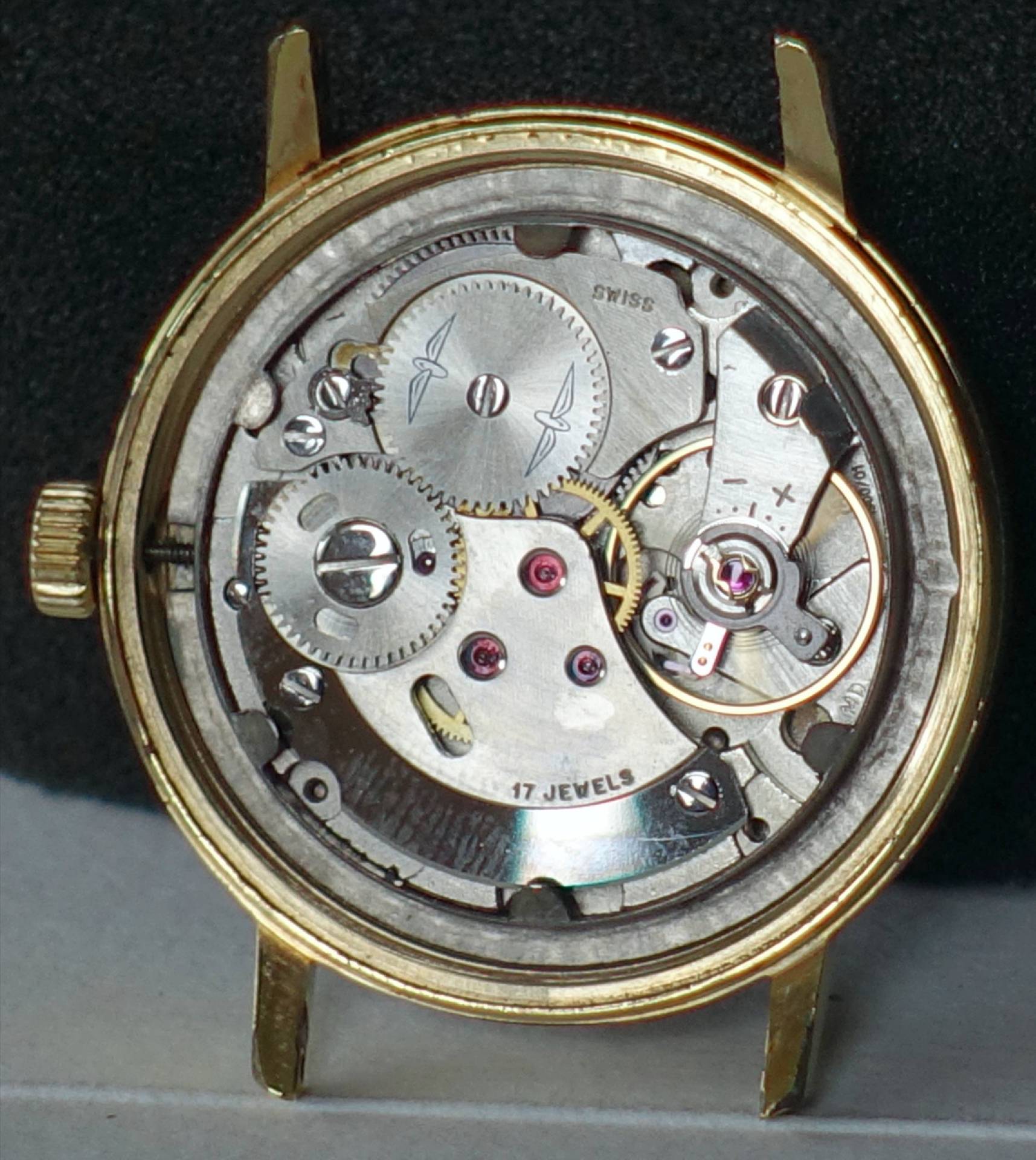 Mechanisches Uhrwerk in einem goldfarbenen Gehäuse mit sichtbaren Zahnrädern und Schrauben.