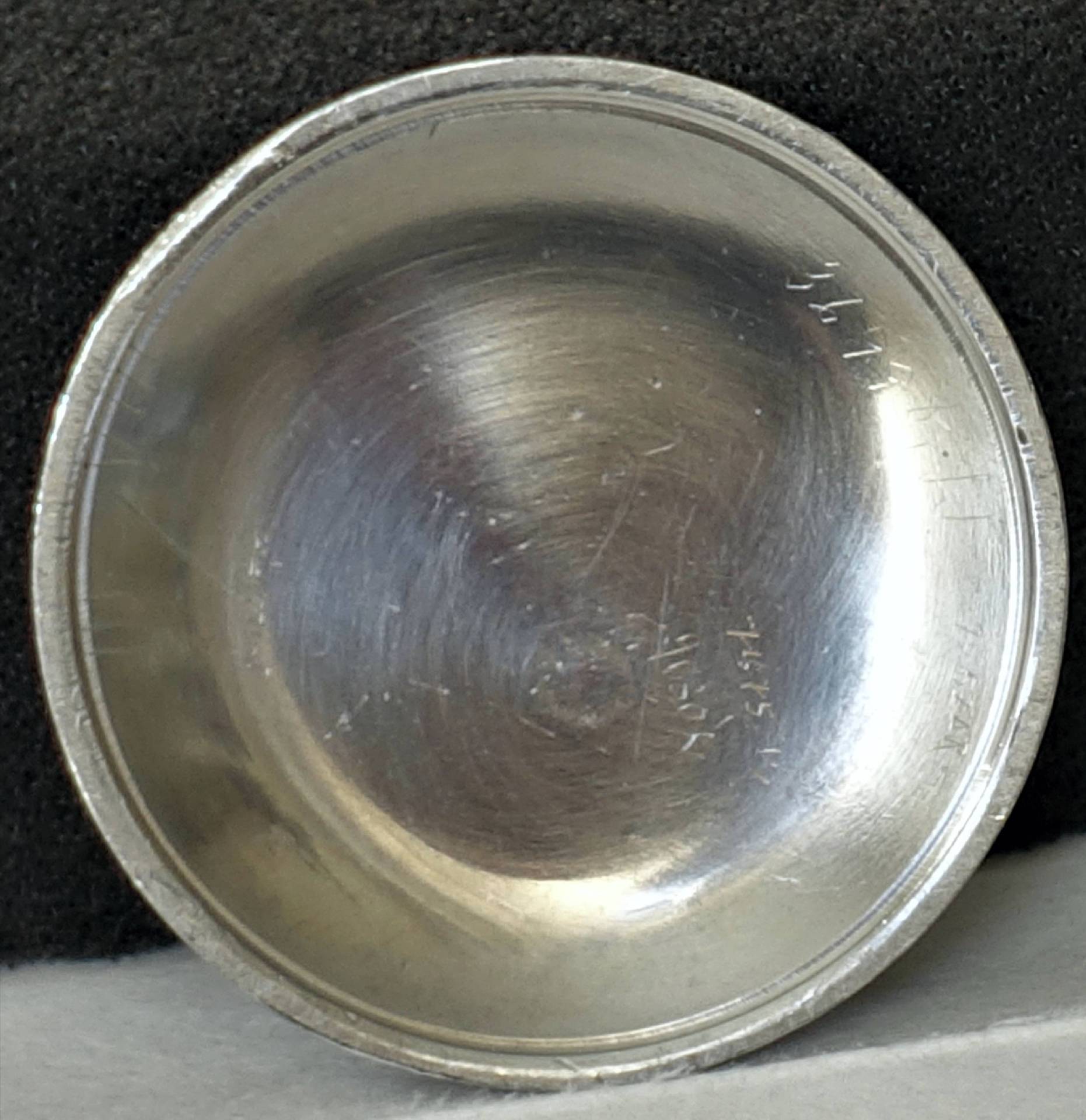 Runder silberfarbener Uhrboden aus Metall mit Gravuren auf der Innenseite.